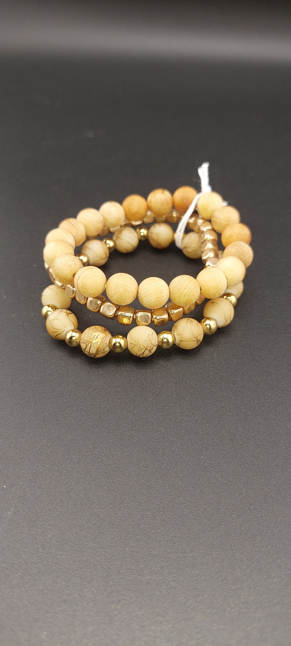 A stack of wooden bracelets with a beige color tone, displayed on a dark background.
