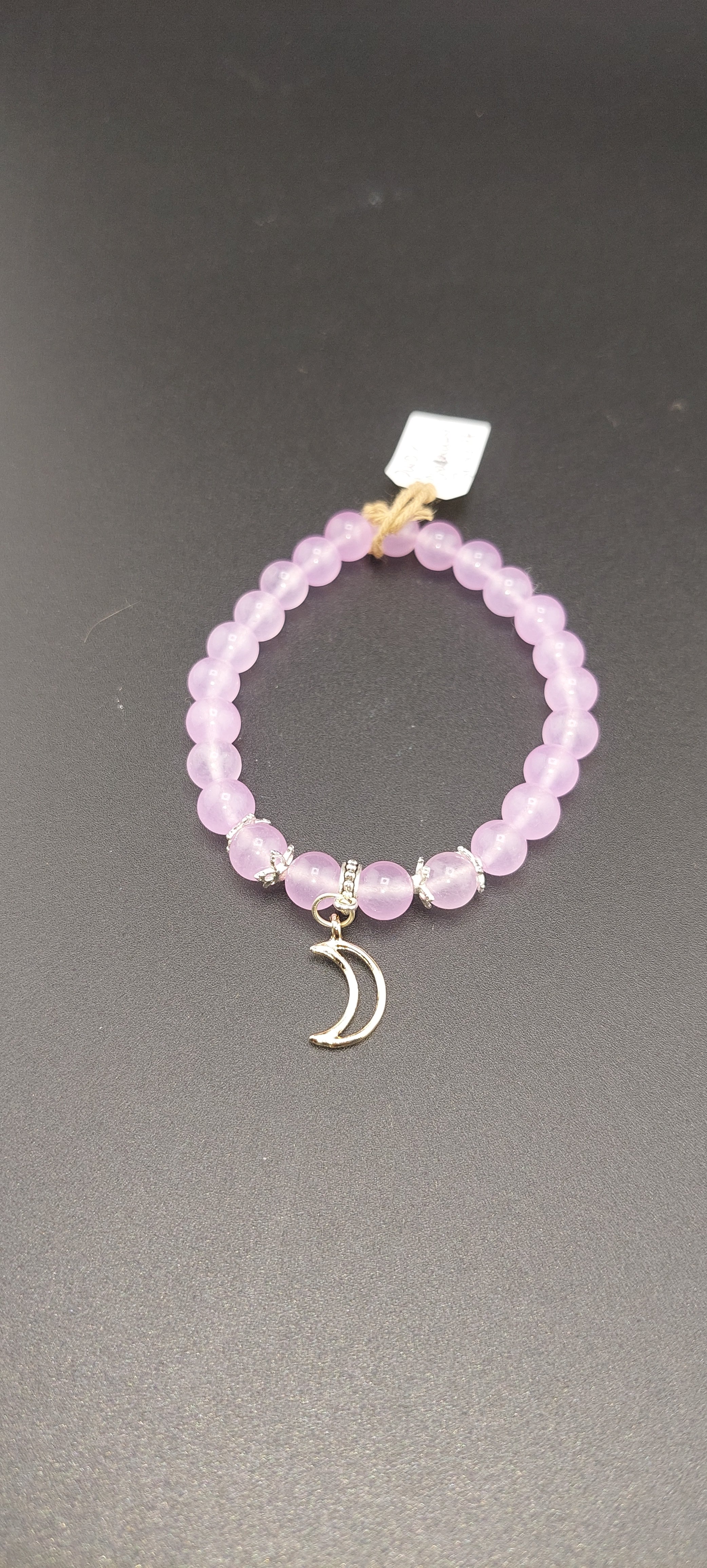 A purple chalcedony bracelet with a crescent moon charm on a dark background.