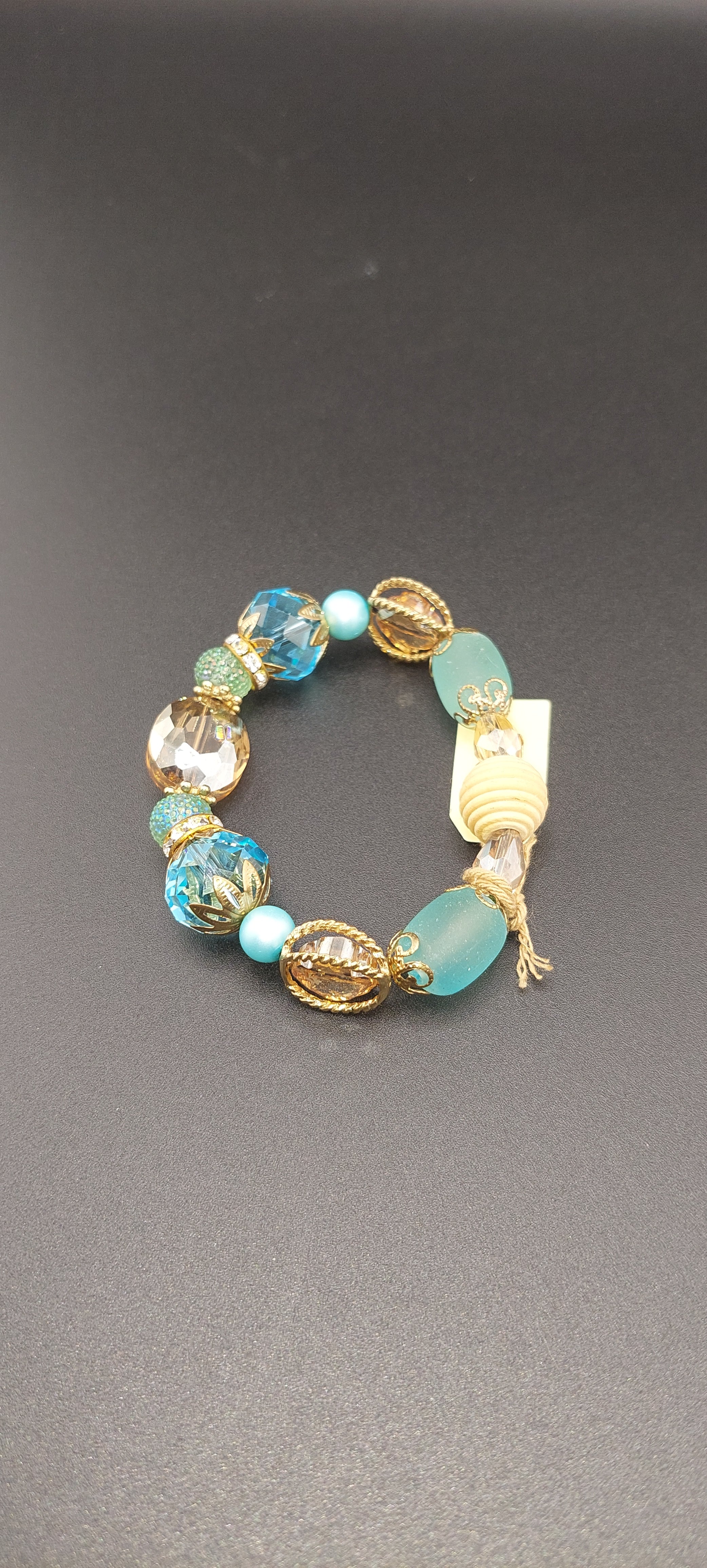 A blue chunky bracelet with gold-colored accents on a dark background.