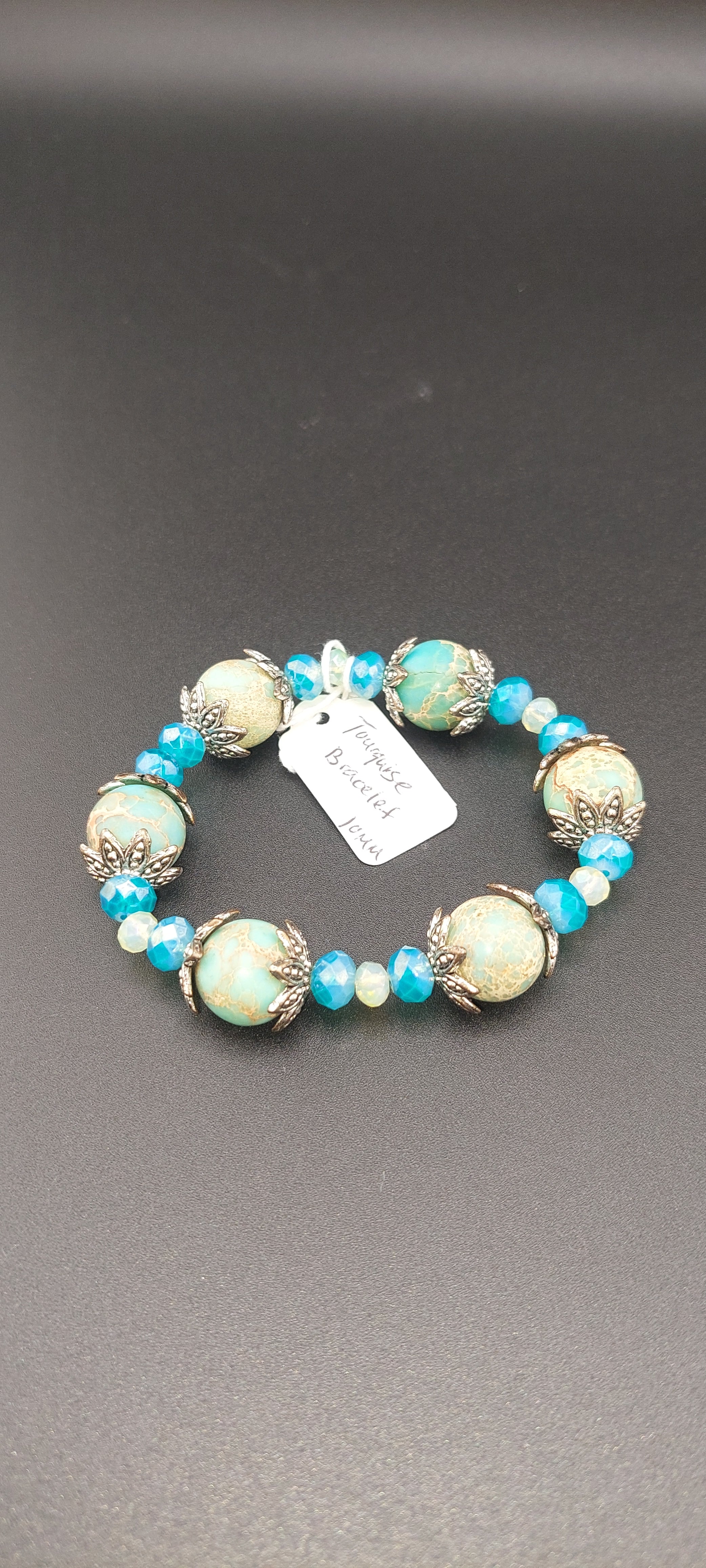 A turquoise bracelet with silver accents and a label attached, displayed against a dark background.