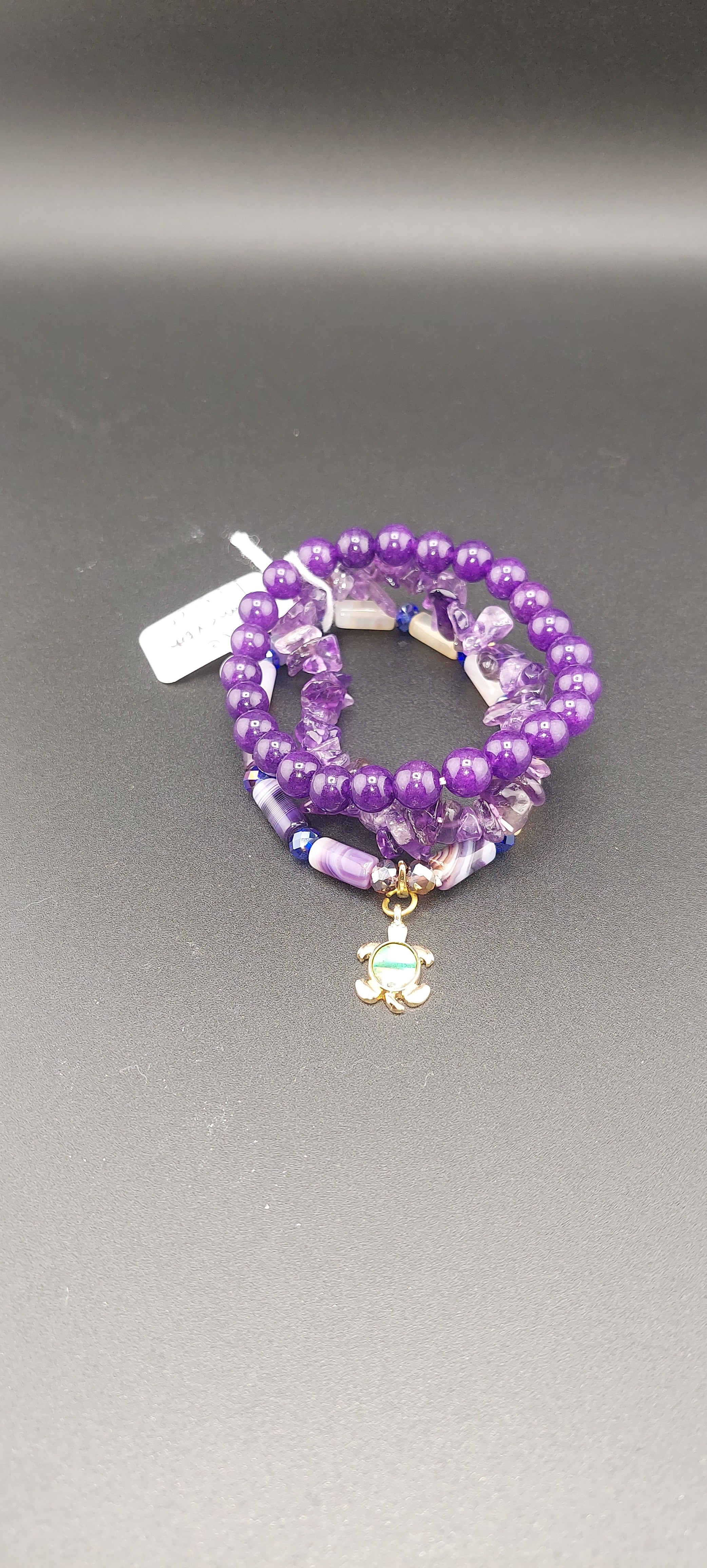 A stack of purple bracelets with a turtle charm