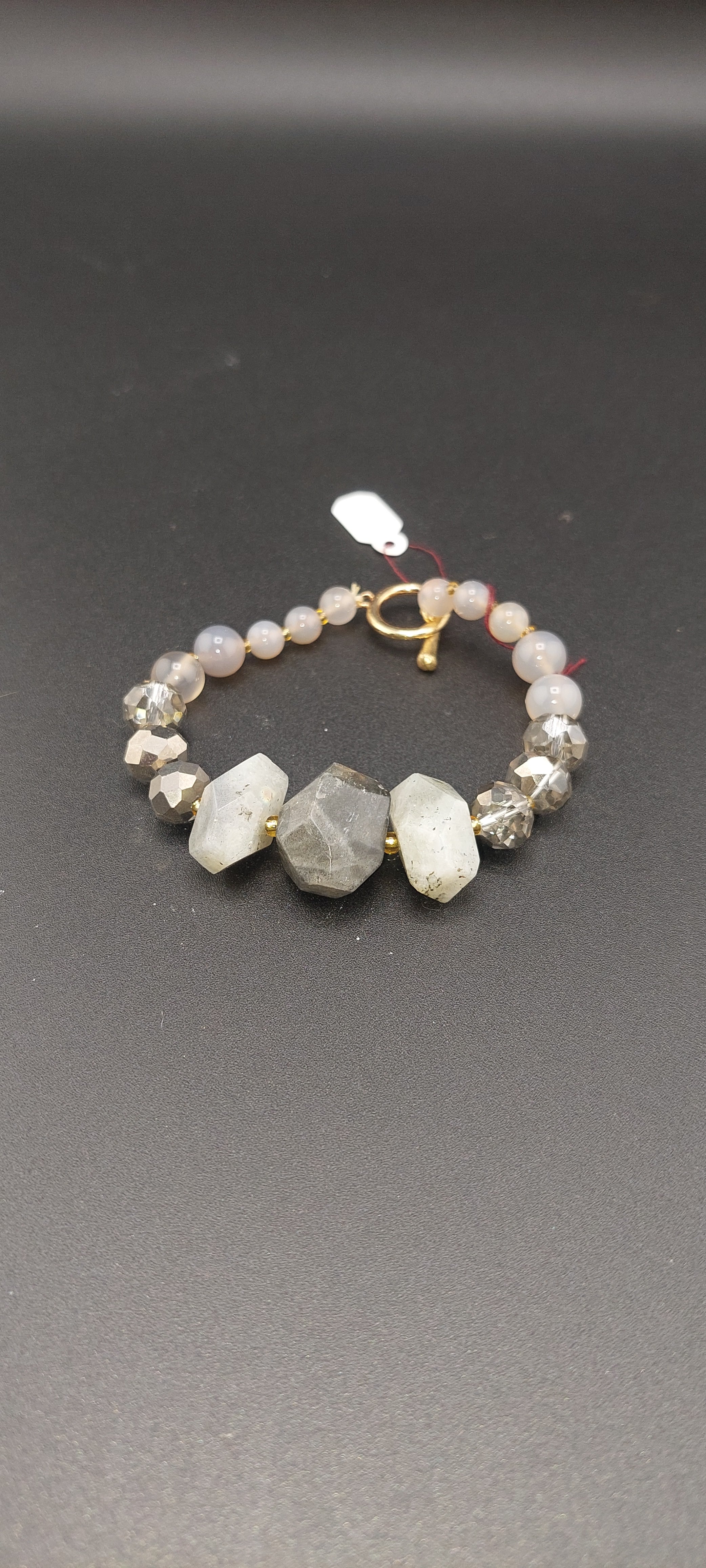 A bracelet with gray quartz crystals and metallic accents on a dark background.