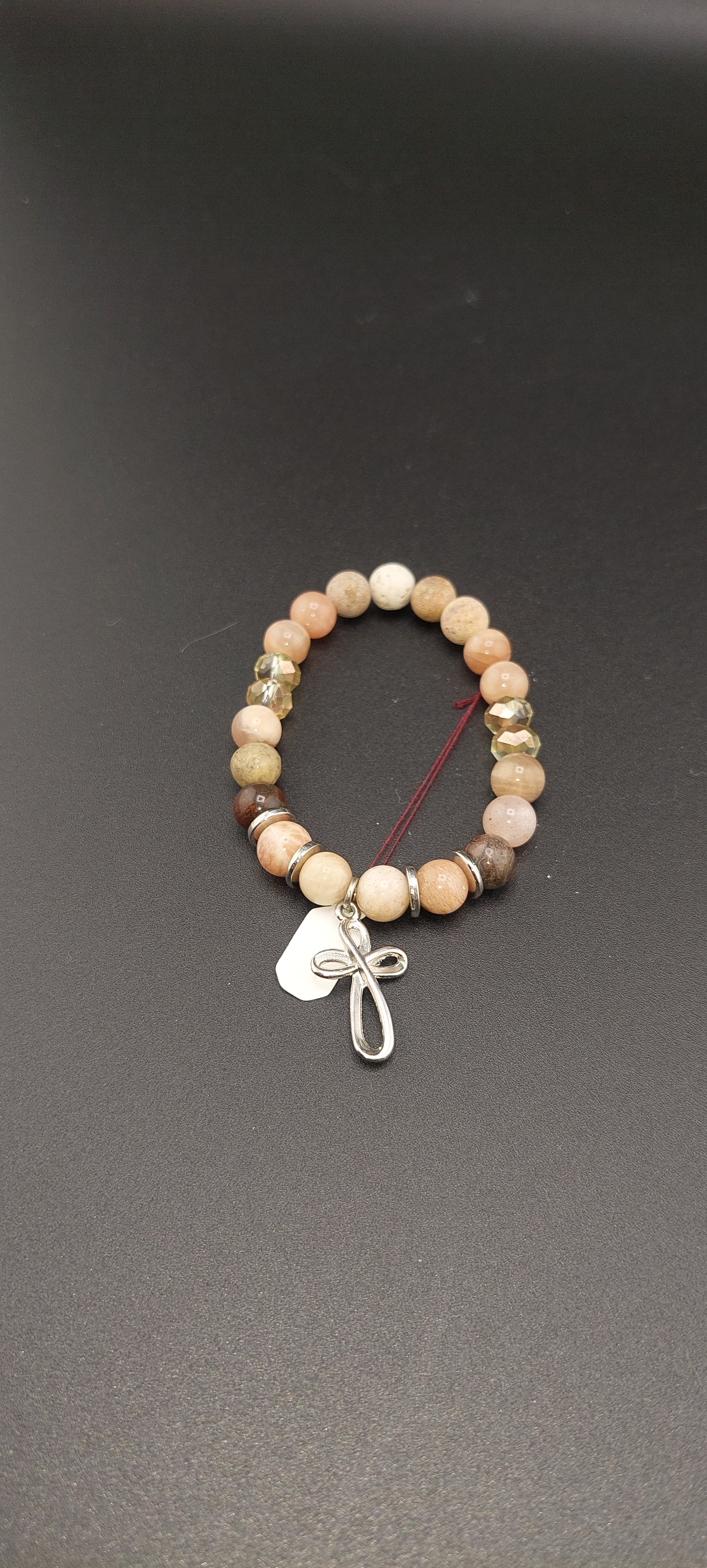 A brown beaded bracelet with a silver cross charm on a dark background.