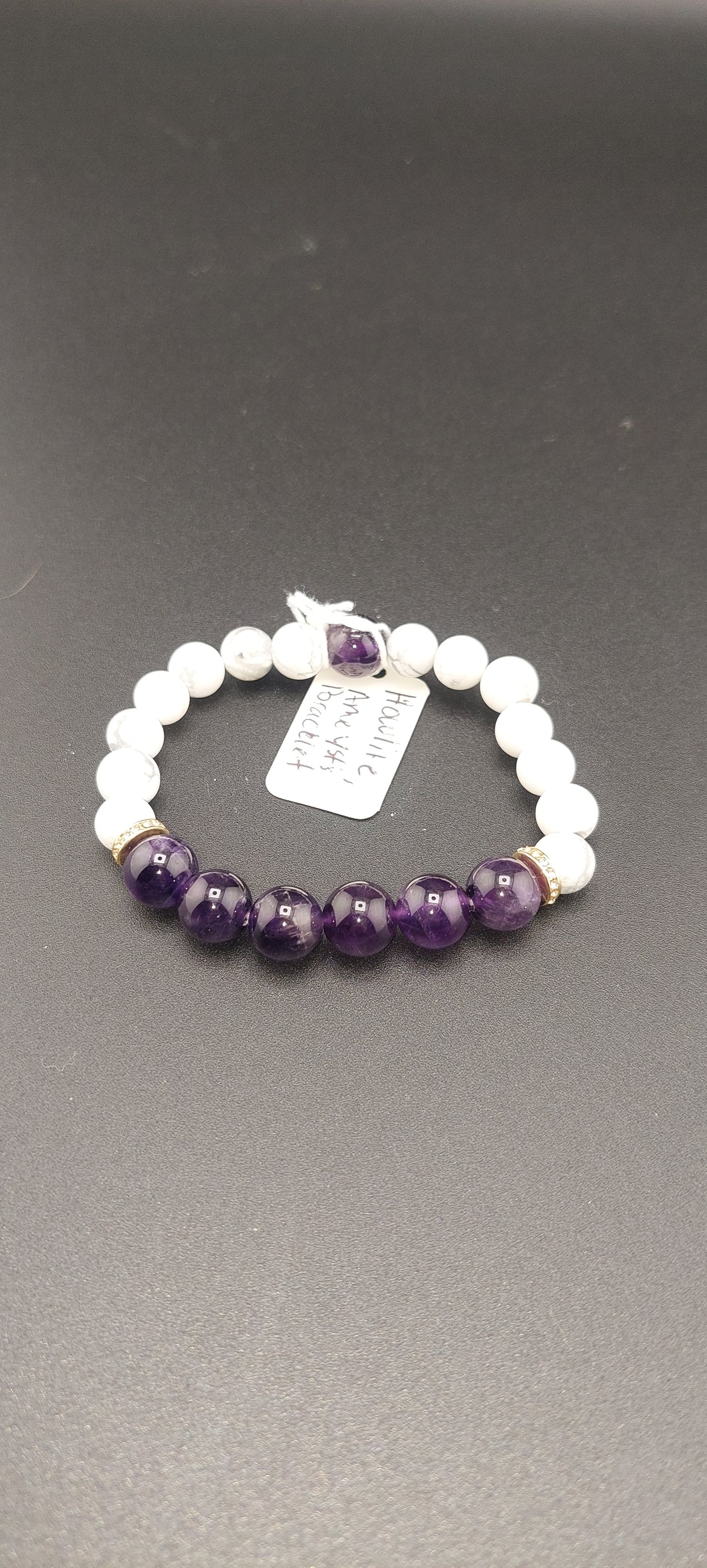 A bracelet with white beads and purple amethyst stones, displayed against a grey background with a price tag attached.