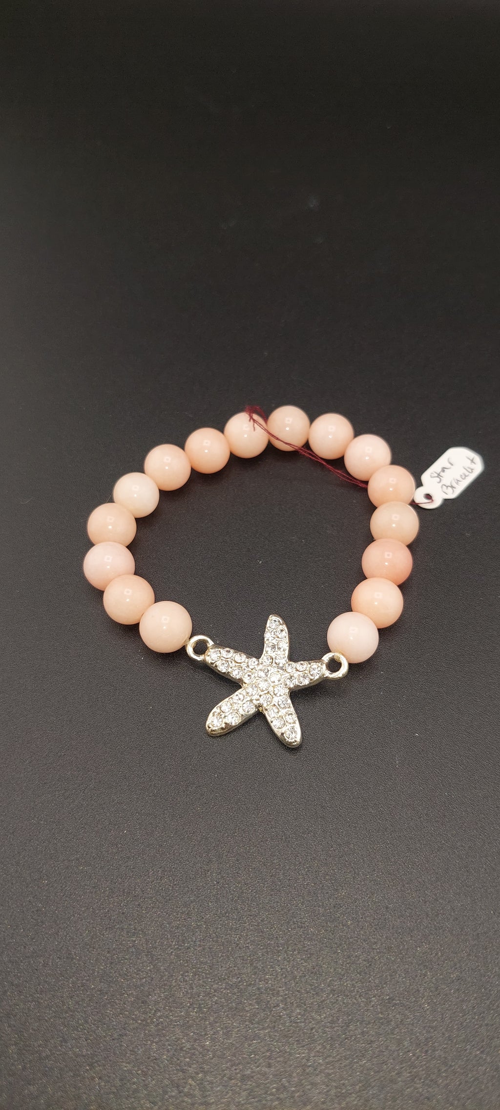 A pink bracelet with a star charm, displayed on a dark background.