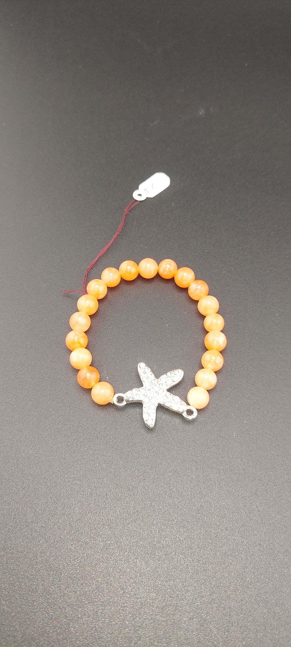 A orange bracelet with a star charm, displayed on a dark background.