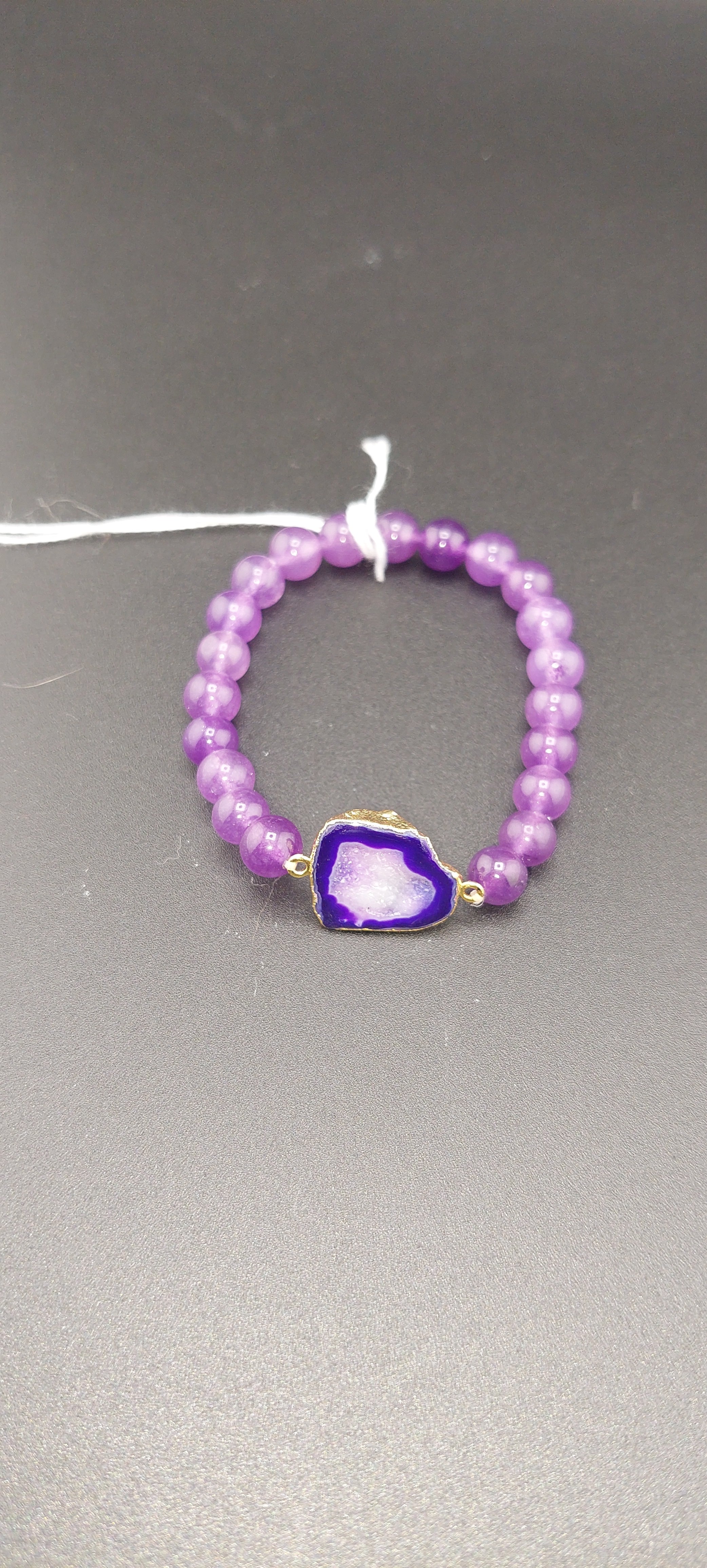 A purple beaded bracelet with a prominent purple drusy crystal in the center, displayed against a neutral background.