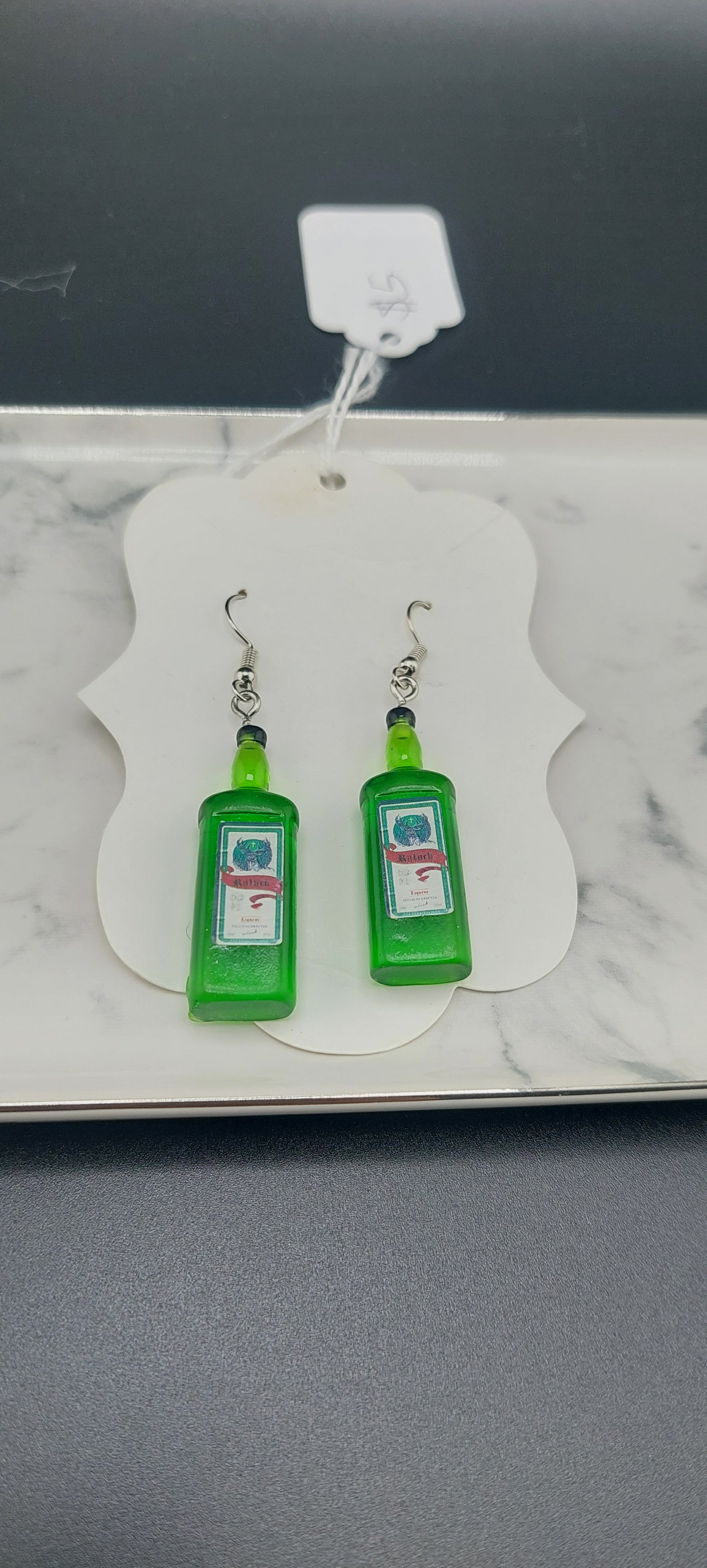 A pair of green earrings with a geometric pattern displayed on a white card, indicating they are meant for retail sale.