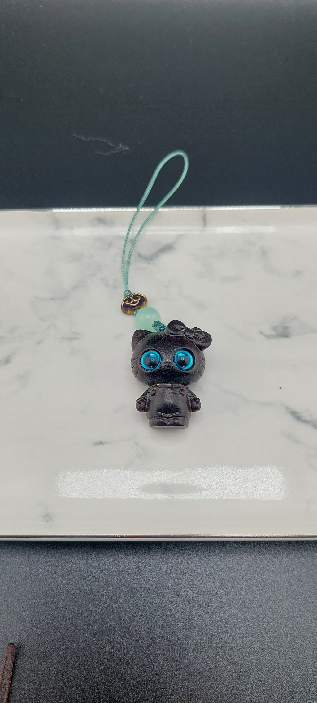 dark wood hello kitty phone and bag charm with dark blue eyes.