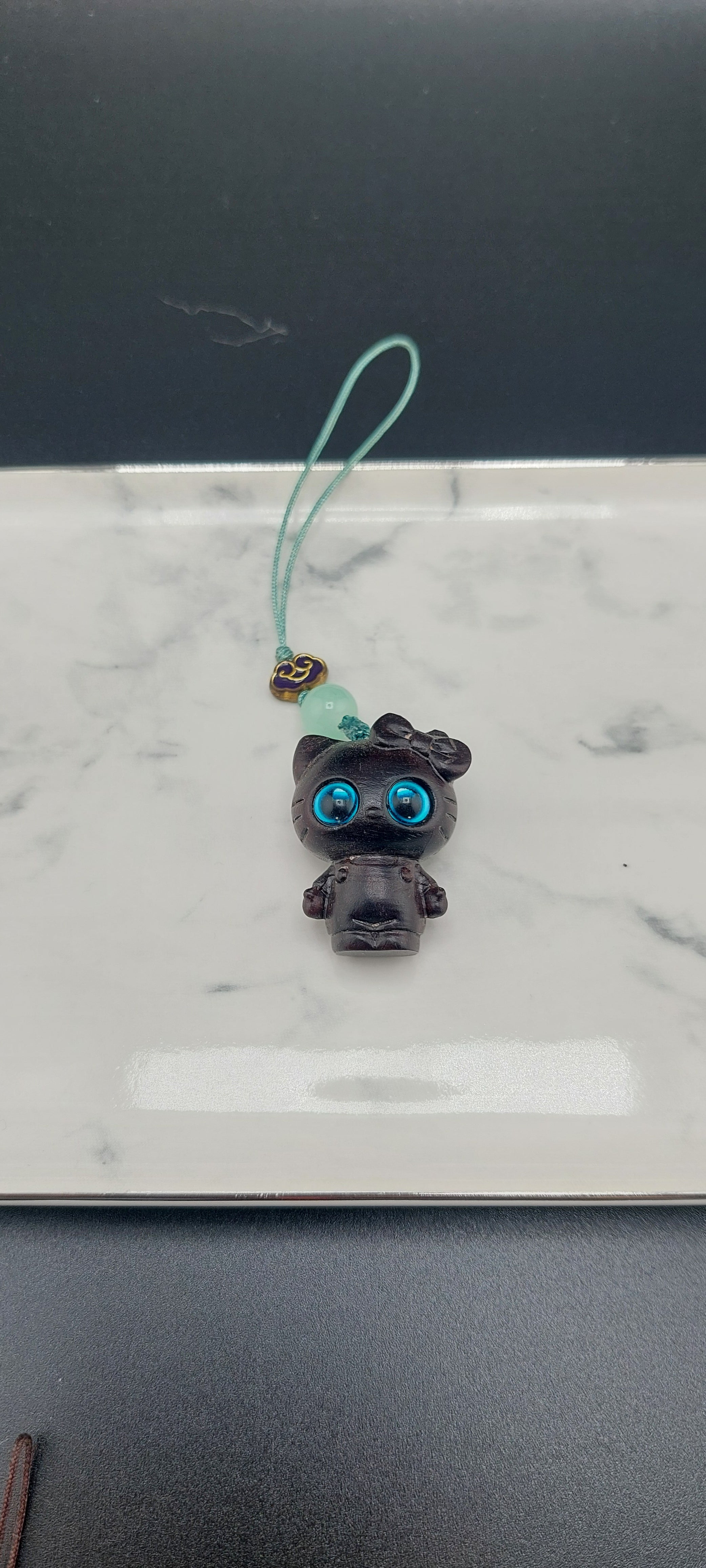 dark wood hello kitty phone and bag charm with dark blue eyes.