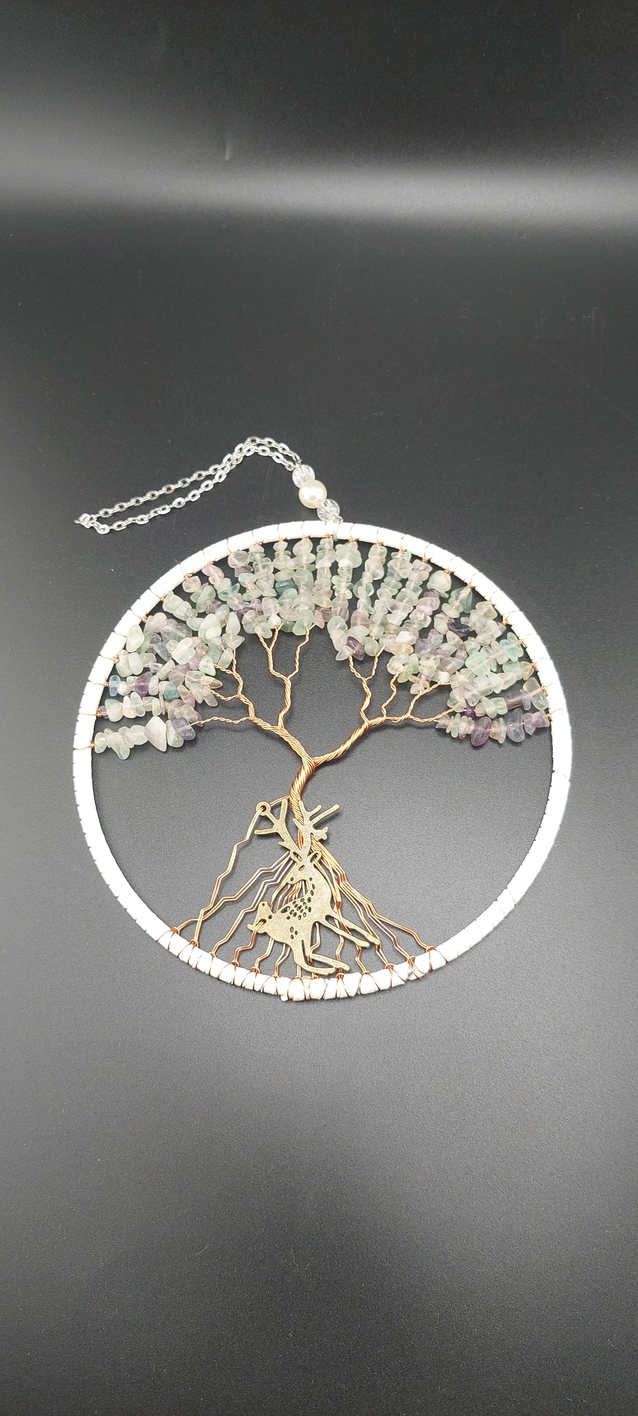 A dream catcher featuring a tree of life design, with white and green stones, and silver wire.