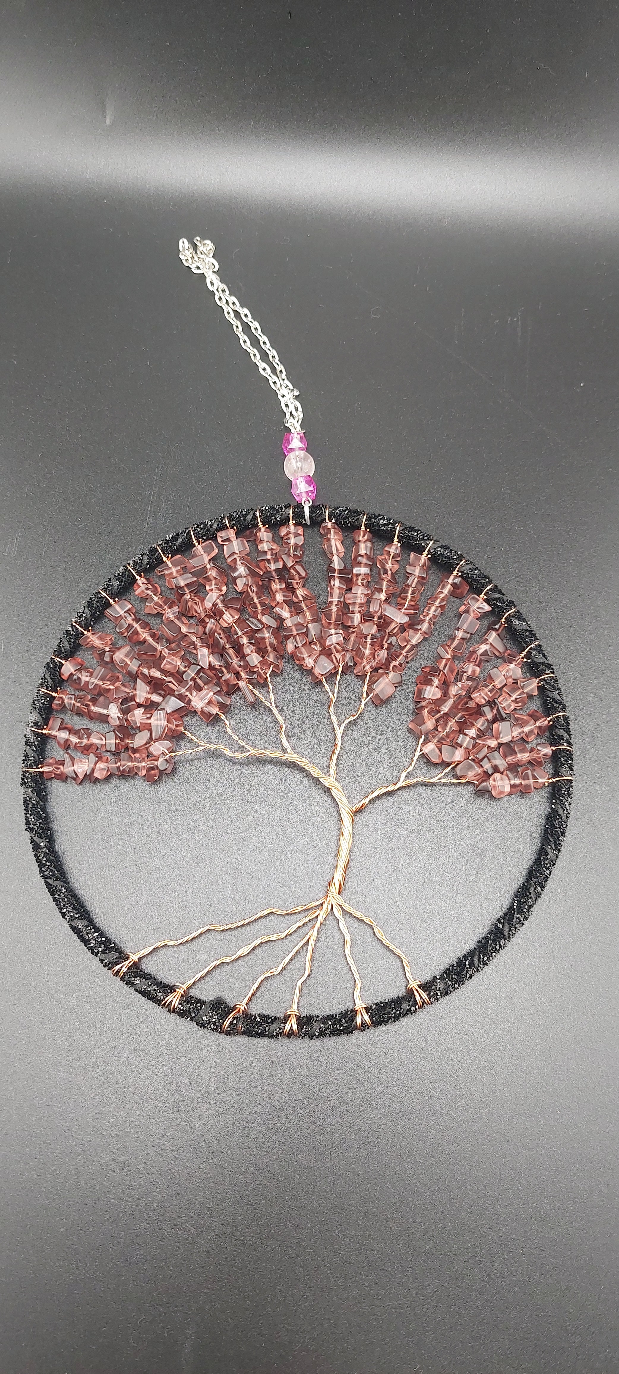 A dream catcher featuring a tree of life design, with black and purple beads, and garnet stones.