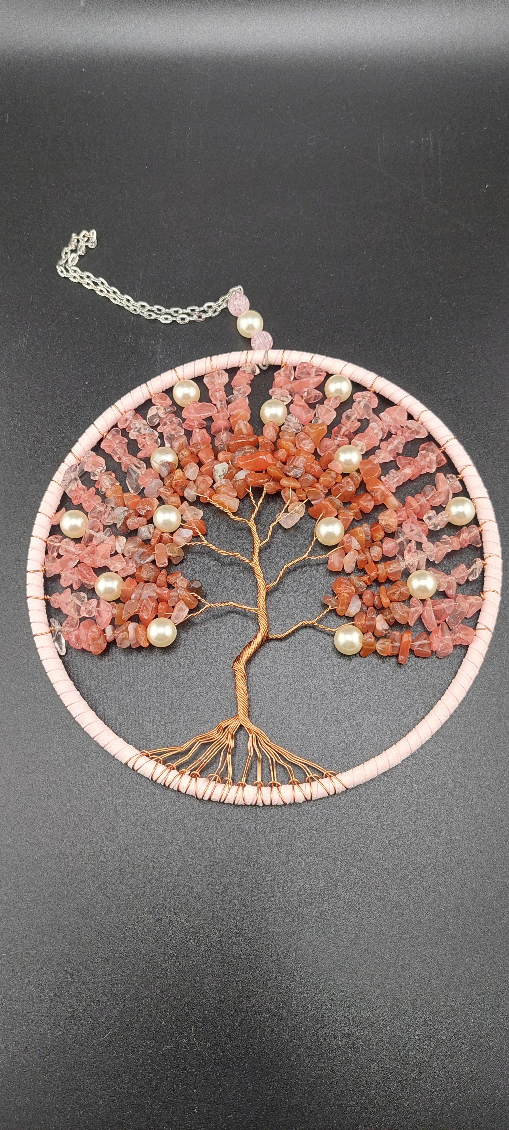 A handcrafted dream catcher featuring a tree of life design, wrapped in wire and adorned with crystals, with a central area made from strawberry quartz.