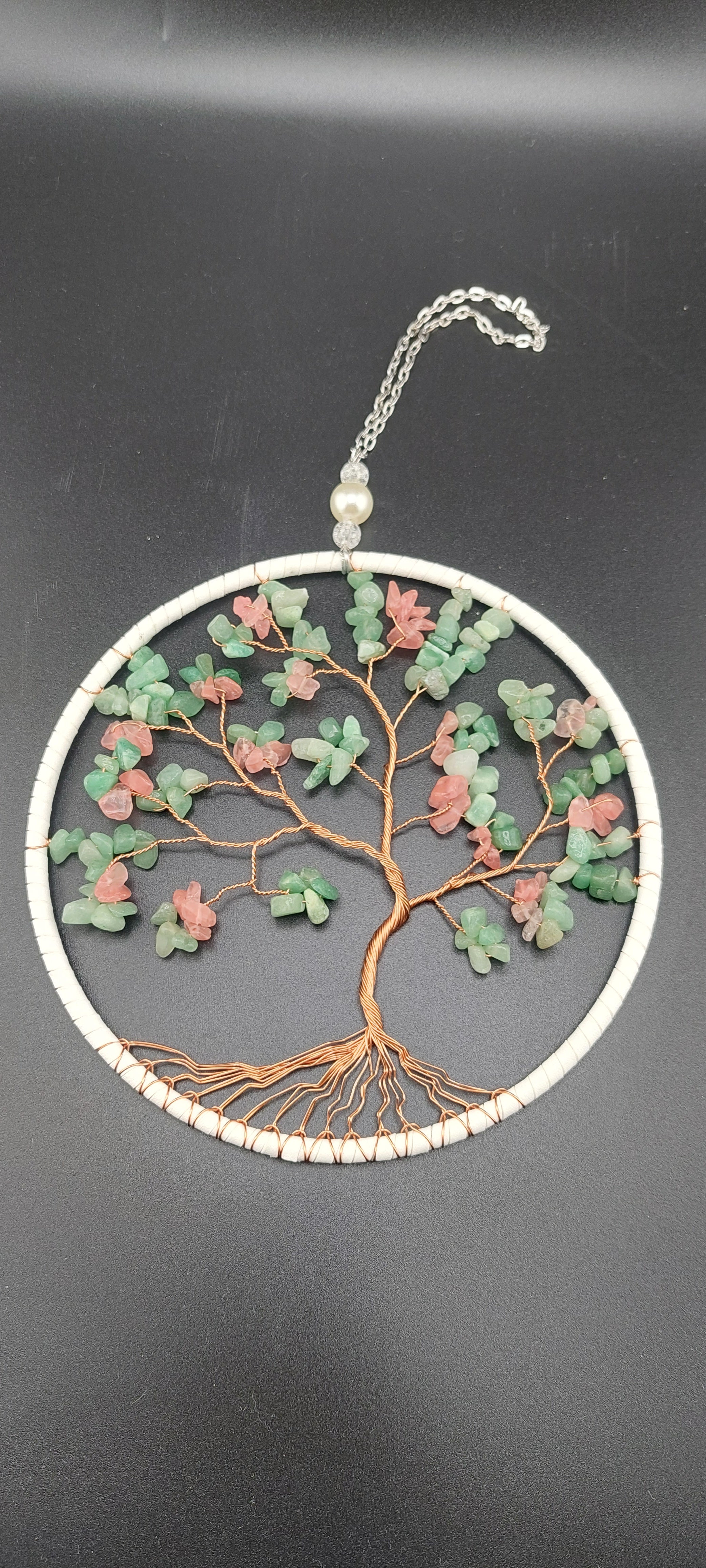 A dream catcher featuring a circular web with leaves made from pink and green chalcedony, and a tree of life design.