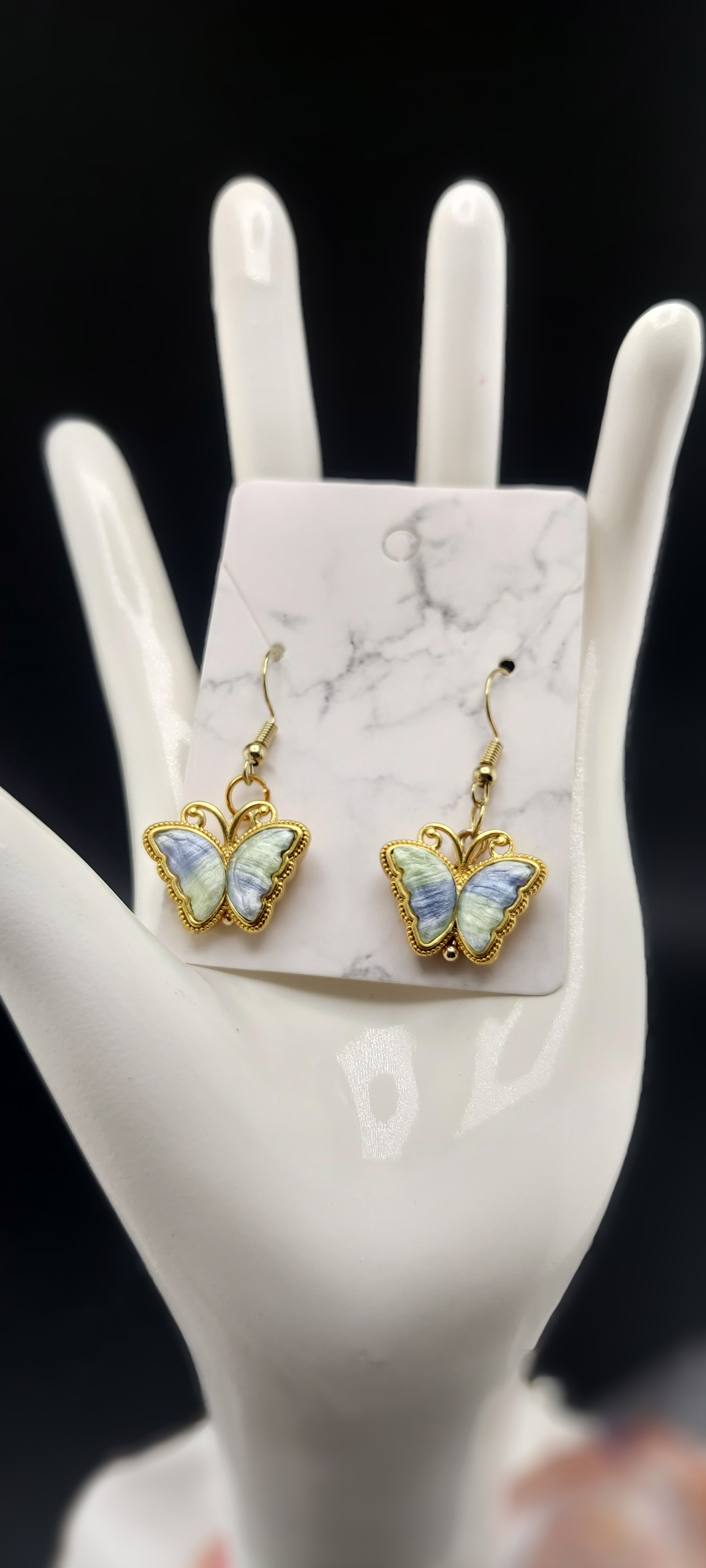 A pair of gold-plated butterfly earrings on a white marble surface.