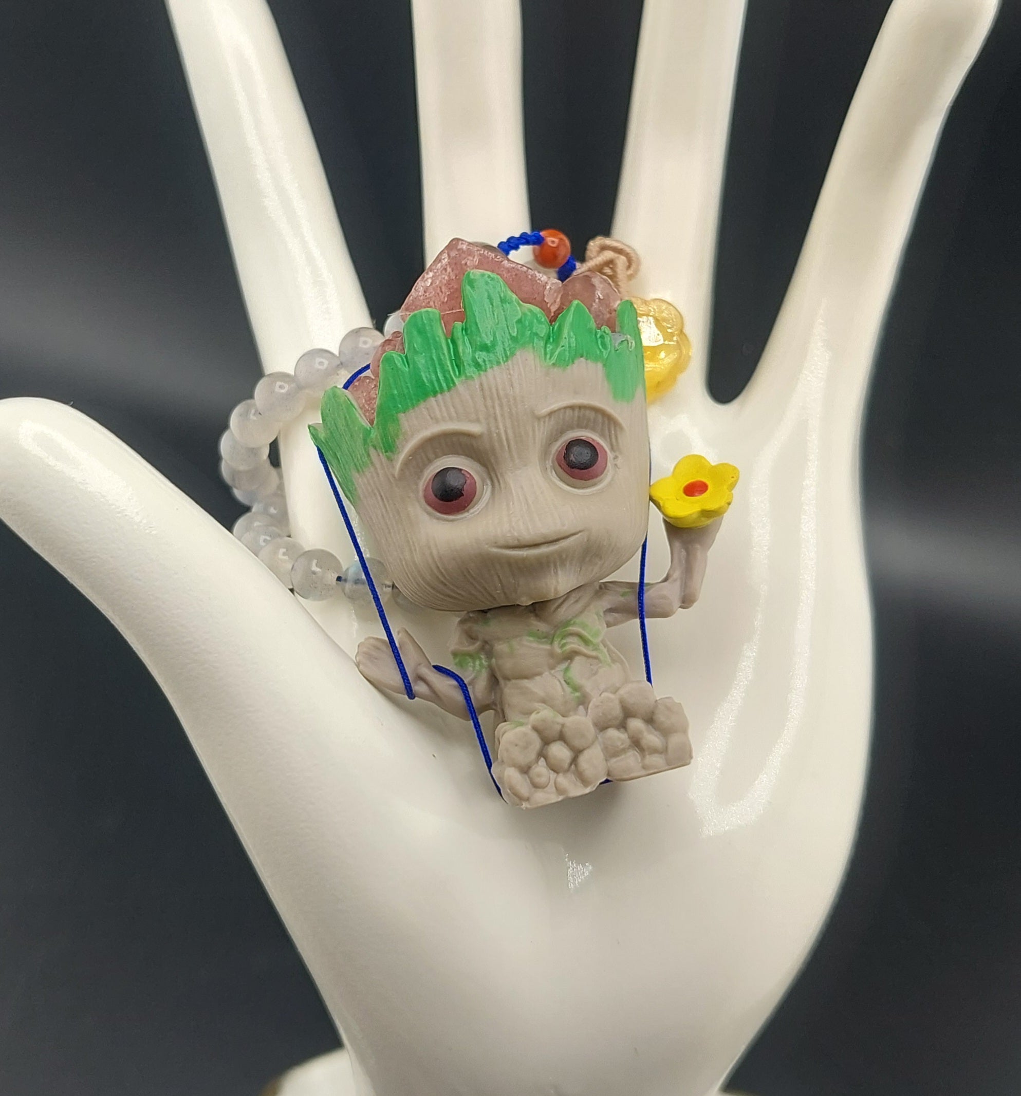 A decorative keychain featuring an animated character styled as a creature with a strawberry quartz body, displayed on a white hand mannequin.