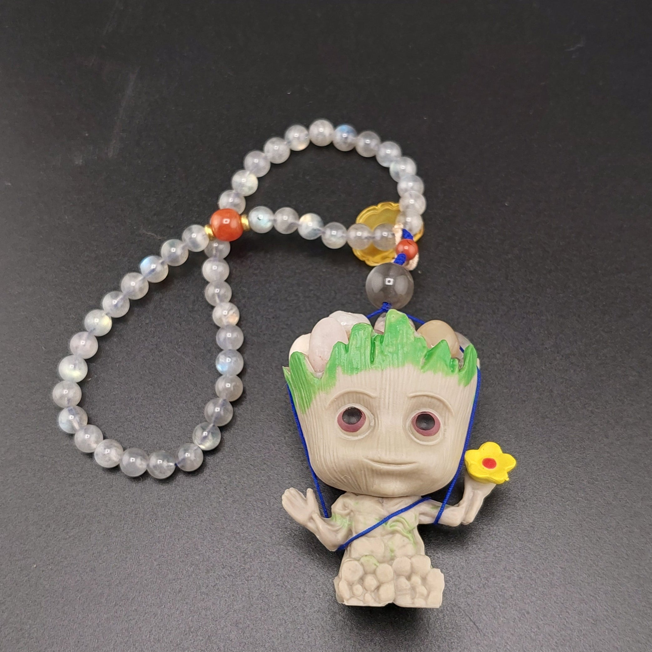 A keychain featuring a small figurine of Groot, with a labradorite stone and flower agate embellishments, attached to a silver-colored ring and chain.