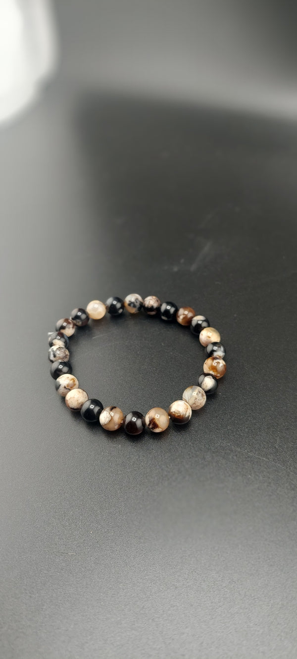 A Black Flower Agate bracelet with round beads, displayed on a grey surface.