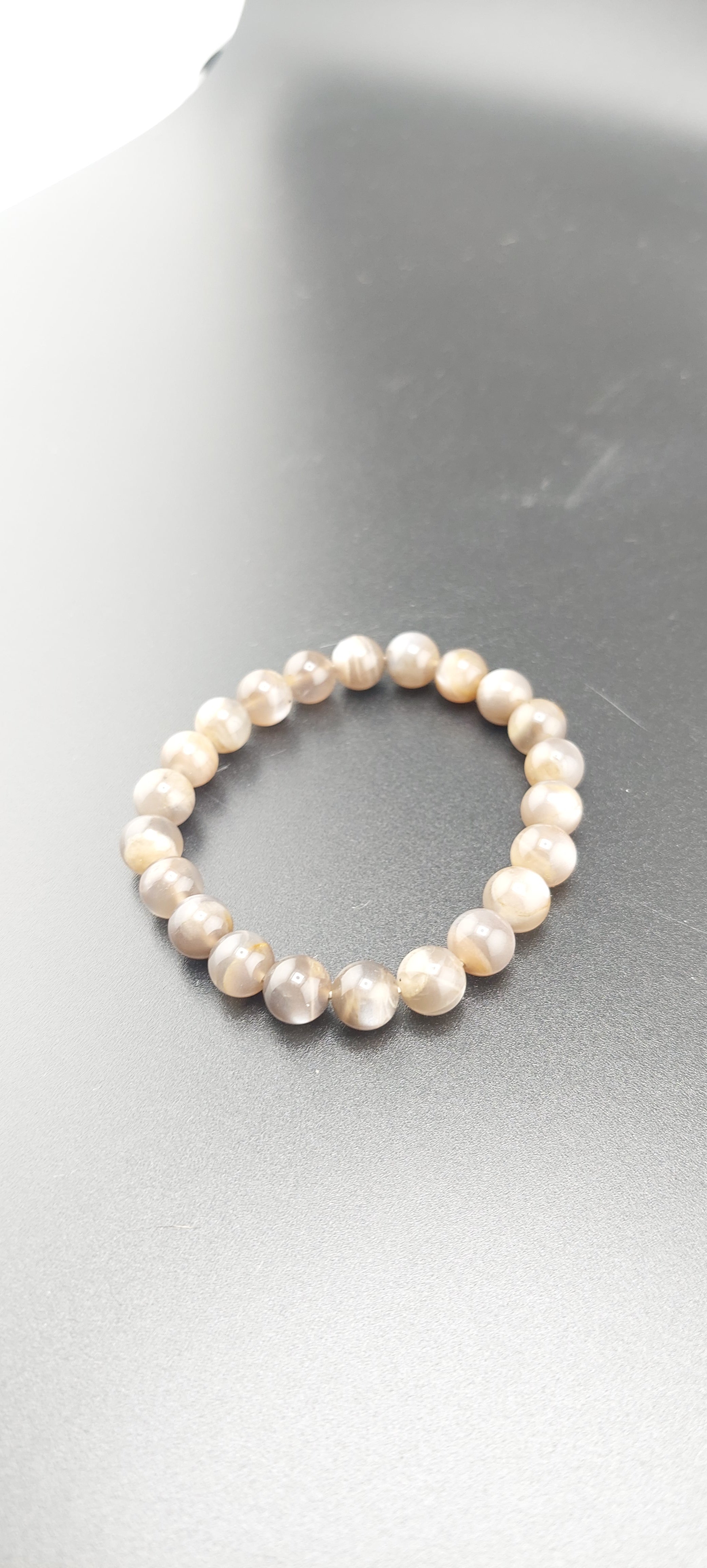 A Peach Moonstone bracelet with light pink beads, displayed on a grey surface.