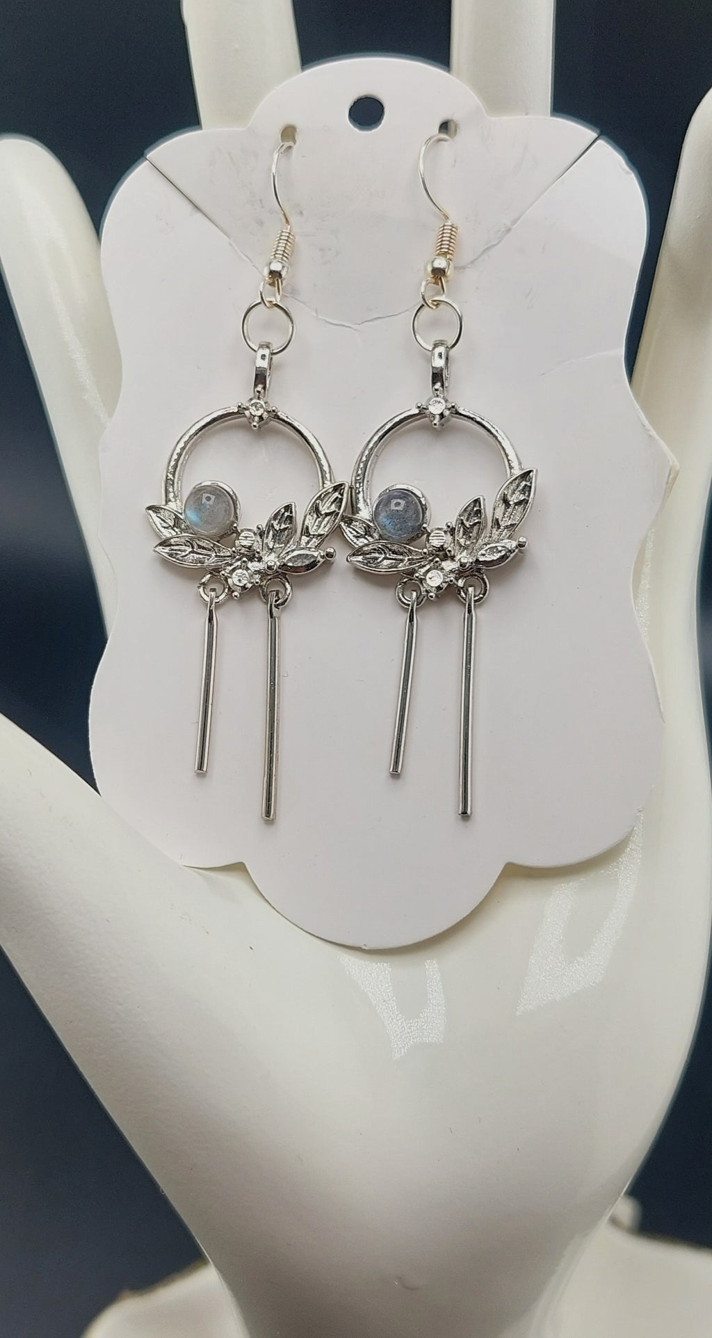A pair of silver-colored flower wreath earrings with purple stones, displayed on a white card.