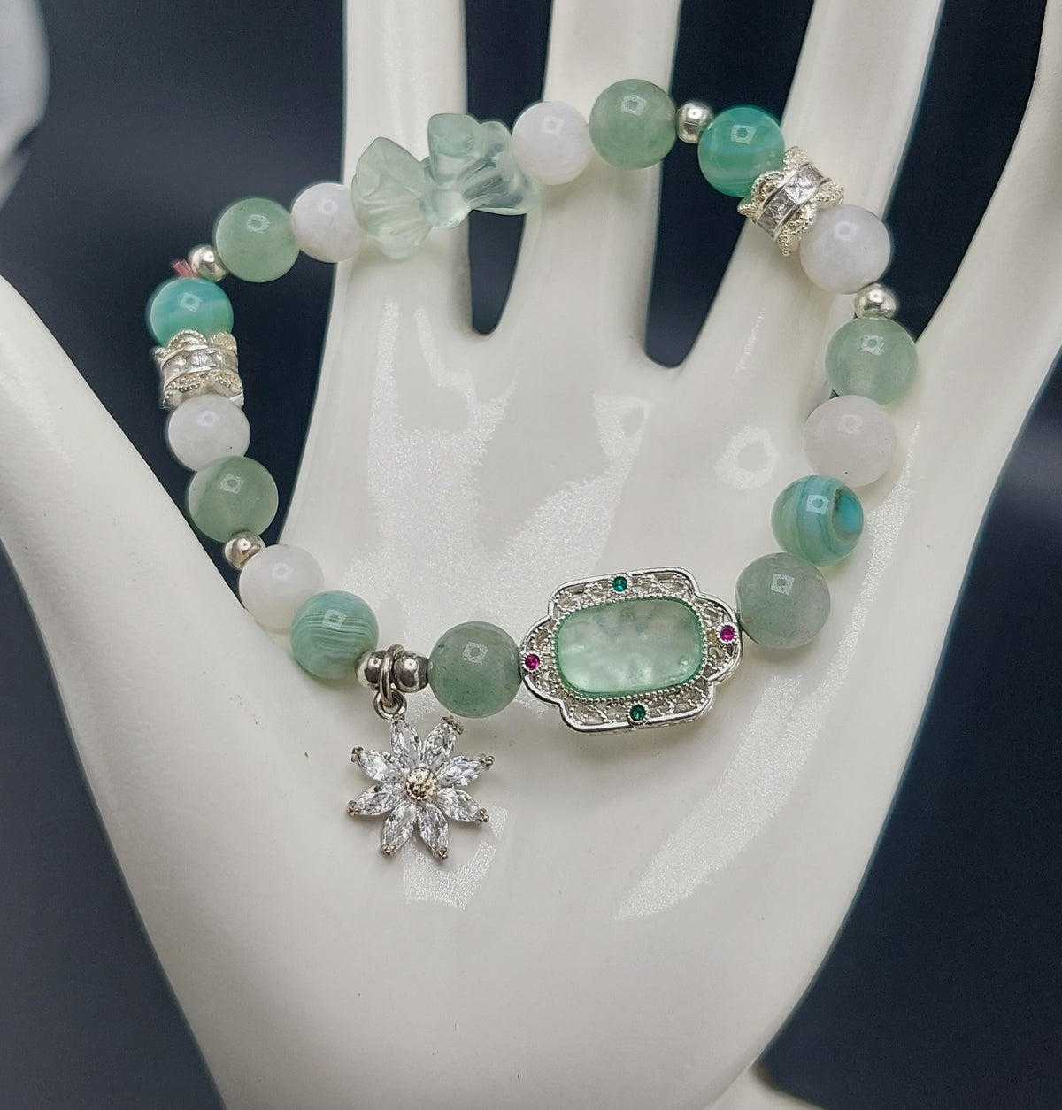 A green bracelet with silver charms and beads displayed on a white mannequin hand.