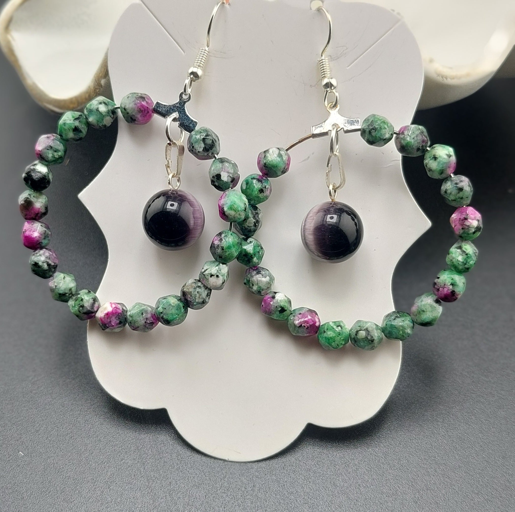 A pair of hoop earrings featuring faceted ruby zoisite stones, displayed against a white background.