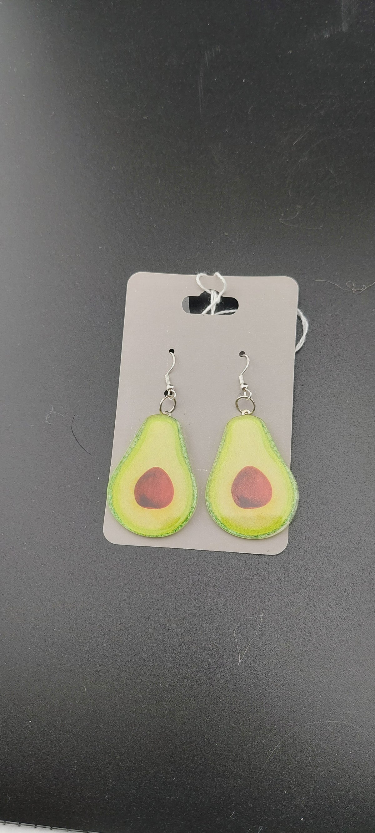 A pair of avocado-shaped earrings displayed on a card, with the earrings in a green color resembling an avocado fruit.