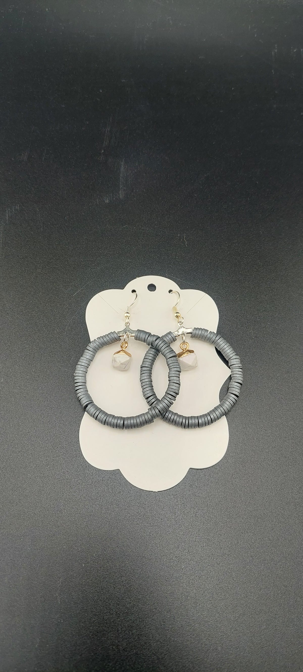A pair of gray hoop earrings displayed on a white holder against a black background.