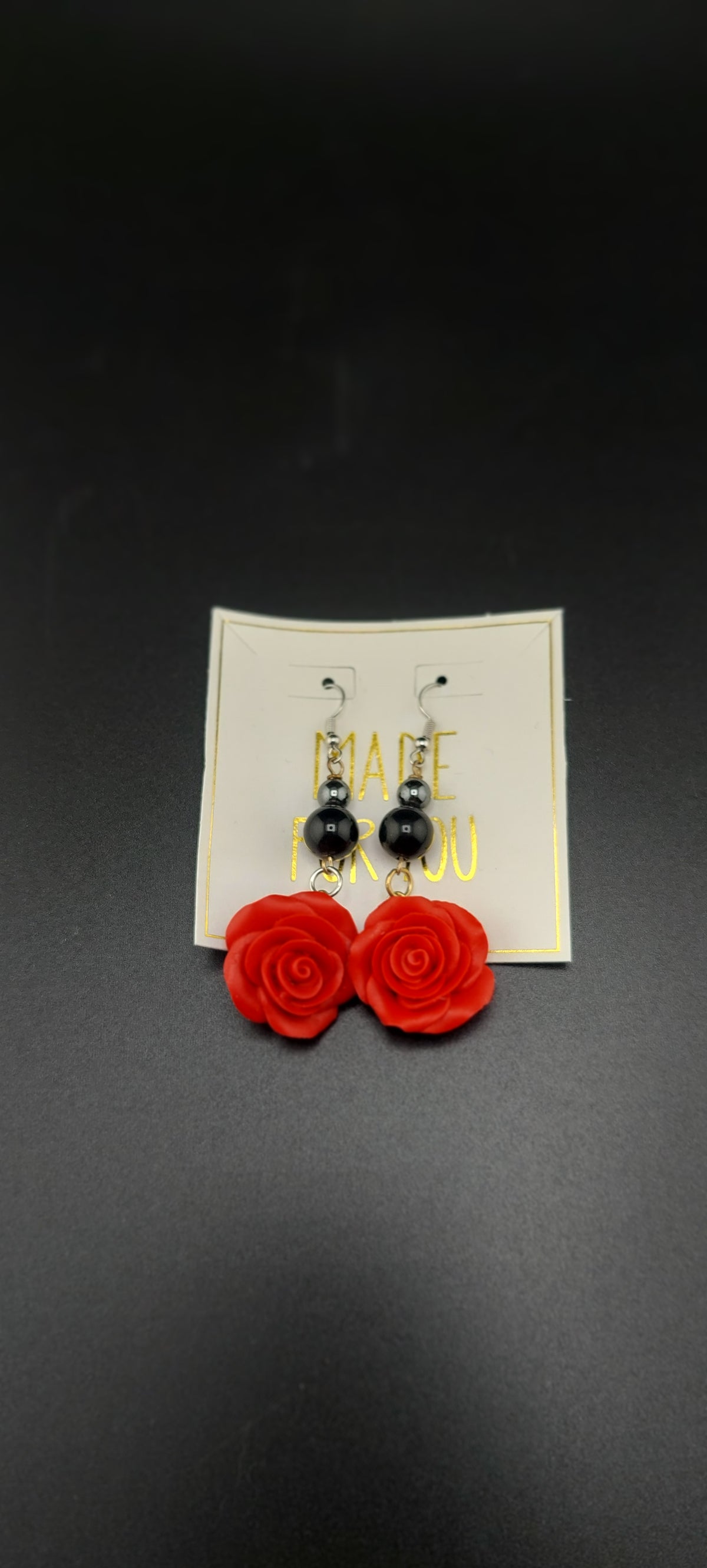 A pair of rose-shaped earrings in red and black colors, displayed on a white card against a black background.