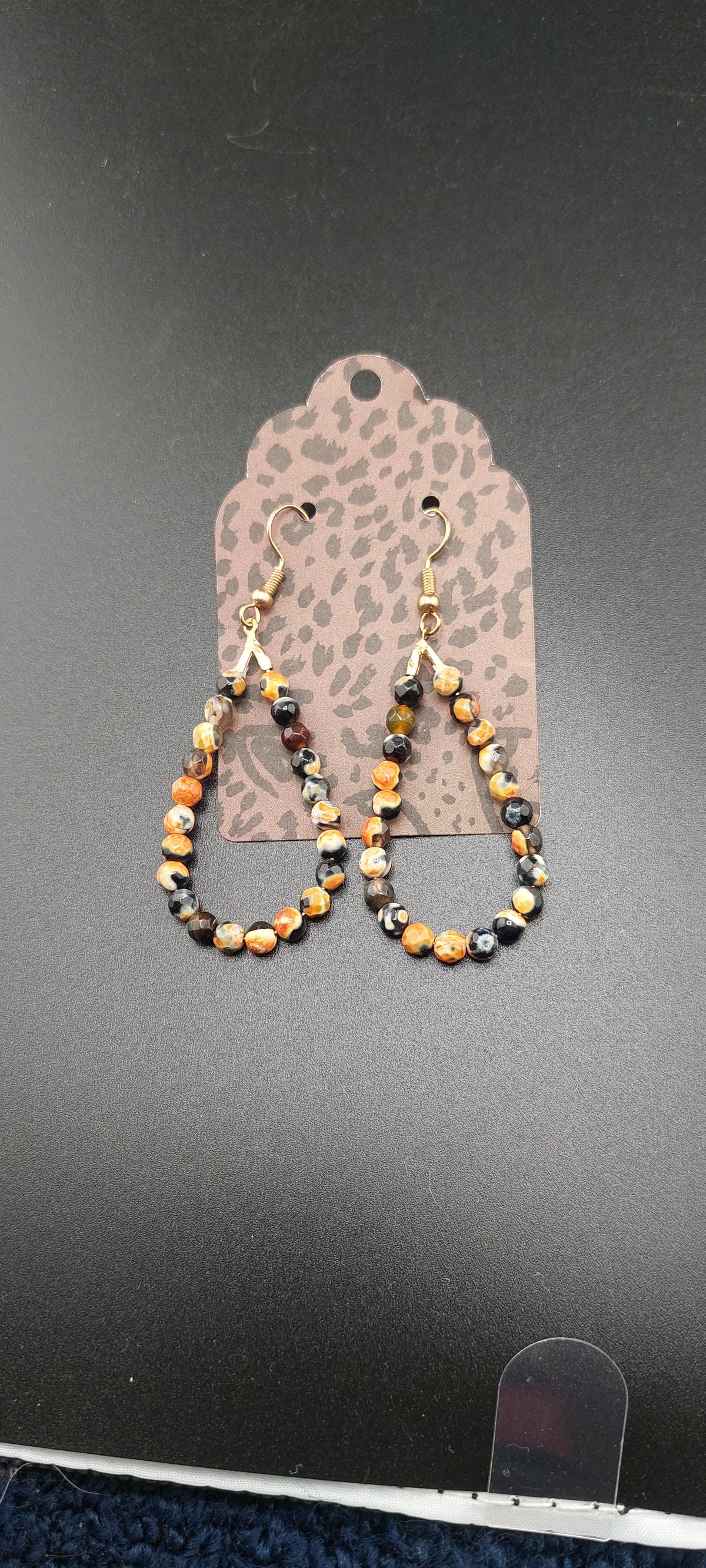 A pair of orange and black beaded earrings designed to resemble orca tears, displayed against a leopard print background.