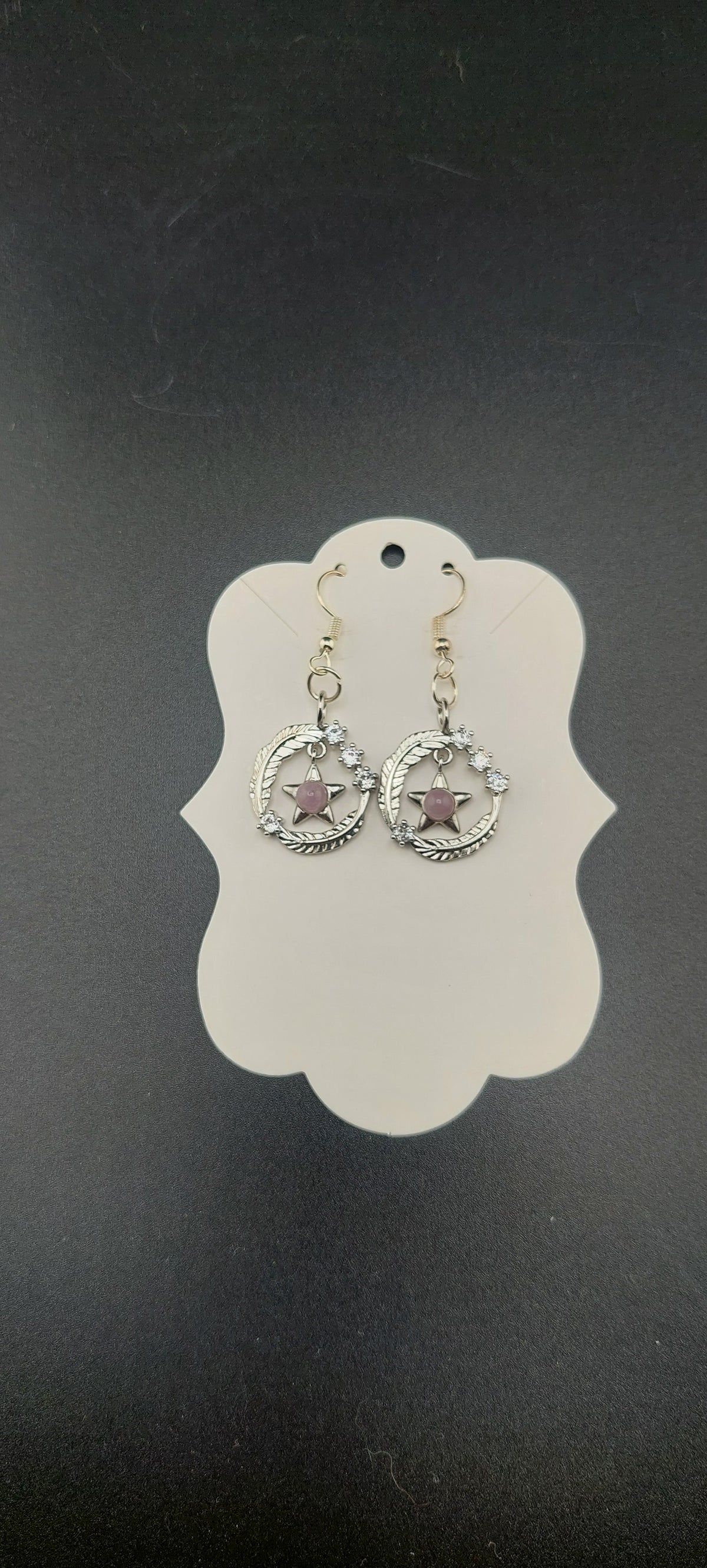 A pair of star earrings on a white display card, with the earrings featuring a gold color and clear crystal-like embellishments.