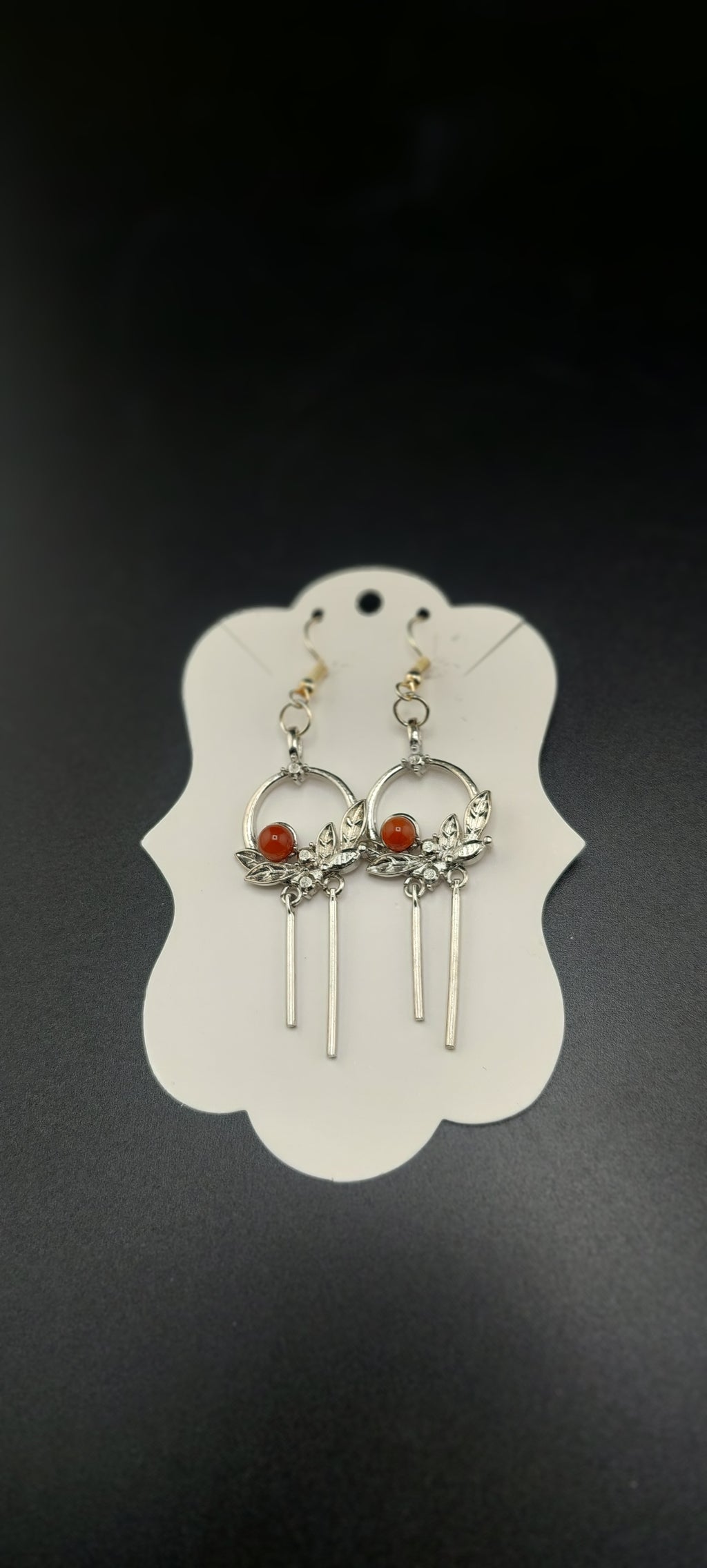A pair of silver-colored flower wreath earrings with purple stones, displayed on a white card.