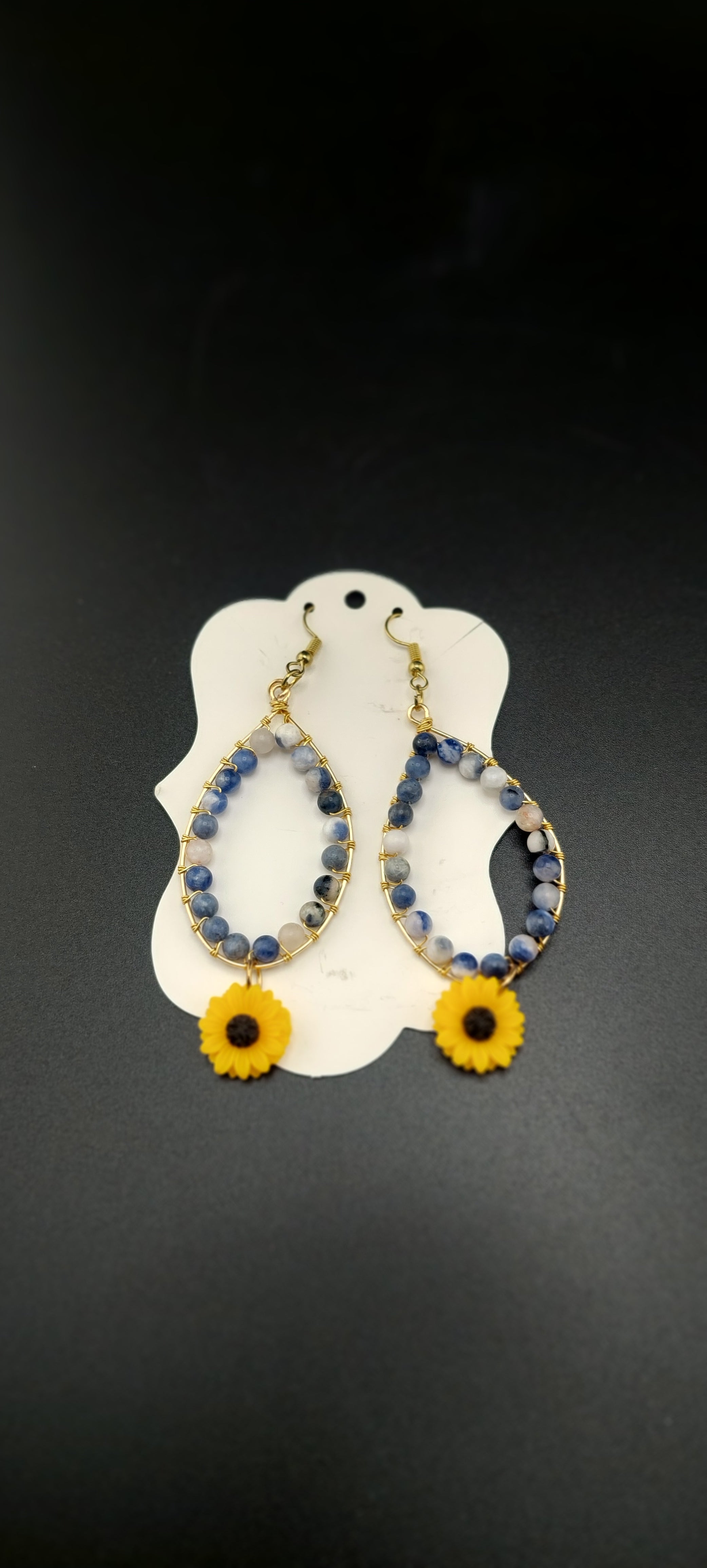 A pair of hoop sunflower earrings displayed against a white background, with the earrings designed to resemble sunflowers with yellow petals and a blue center.