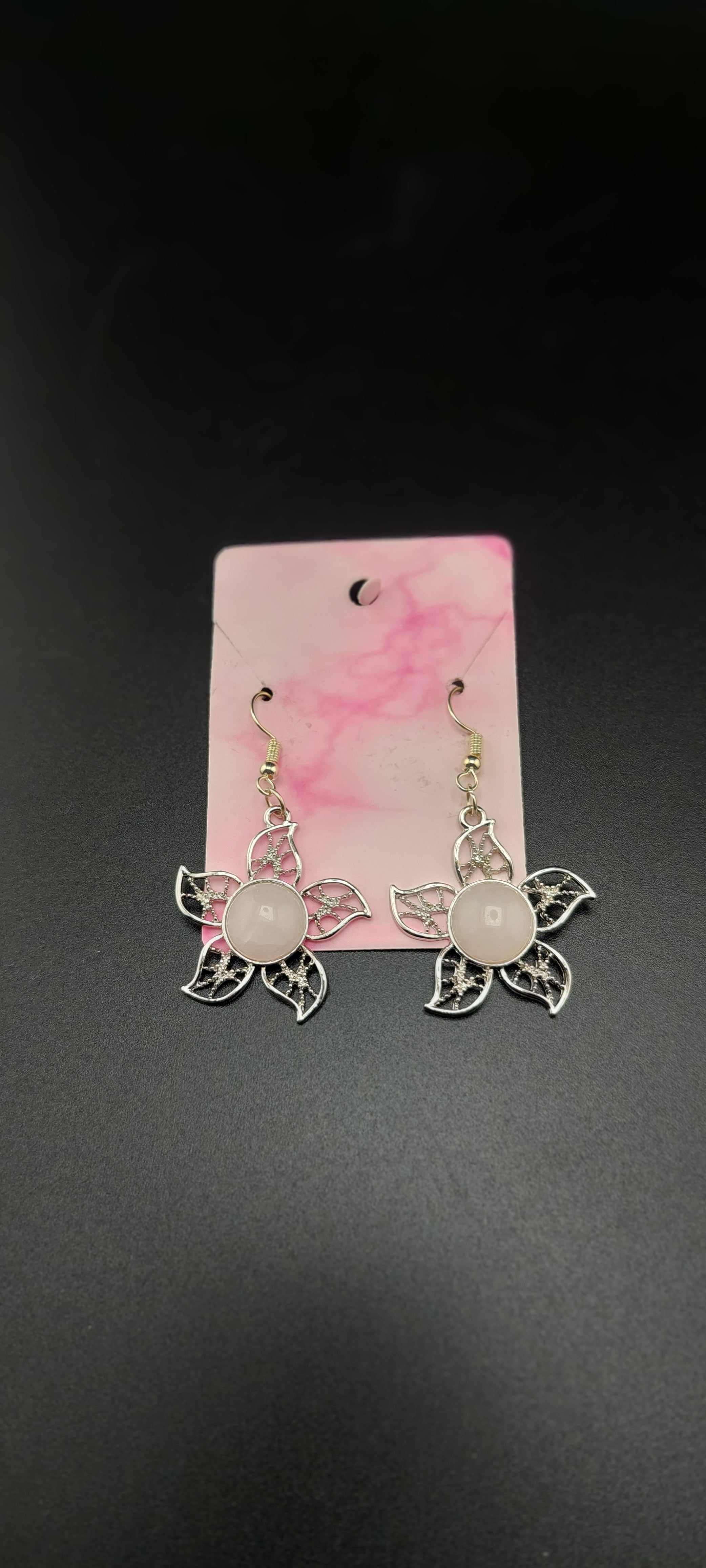A pair of rose quartz flower earrings displayed on a pink card against a black background.