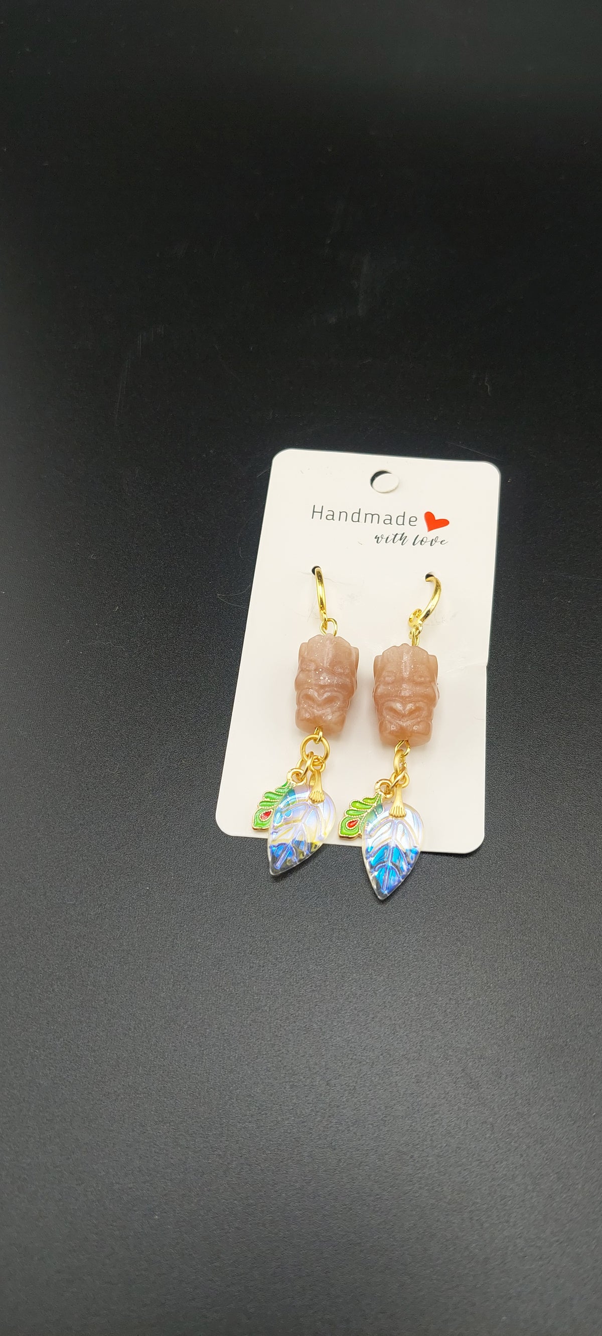 A pair of earrings featuring peach moonstone beads, displayed on a white card with a printed logo.