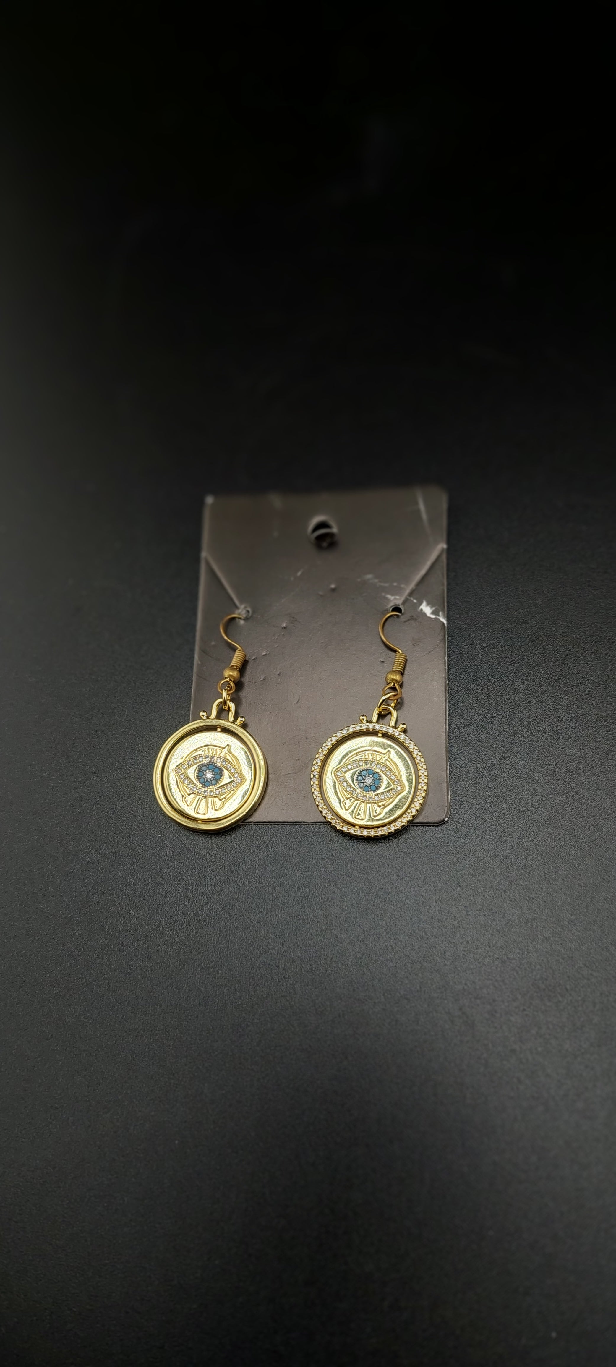 A pair of eye of Horus earrings displayed against a black background, featuring gold-colored outlines around the earrings.