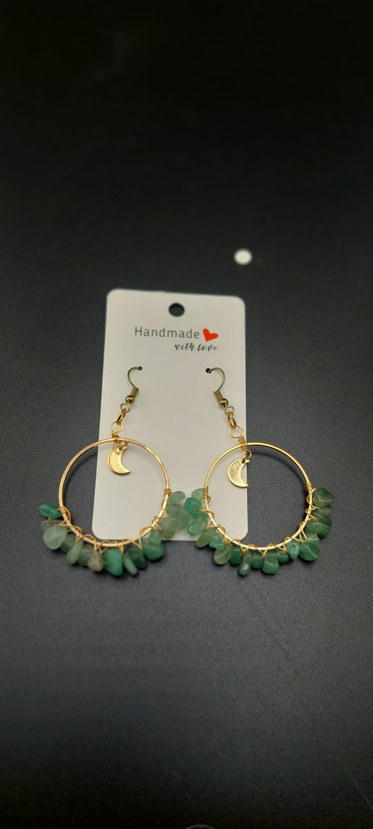 A pair of gold-colored hoop earrings with blue wire wrapping and dark blue beads, displayed on a white stand.