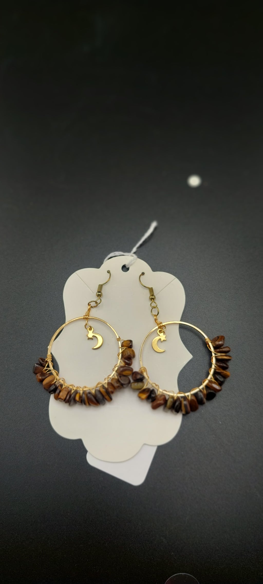 A pair of gold-colored hoop earrings with blue wire wrapping and dark blue beads, displayed on a white stand.