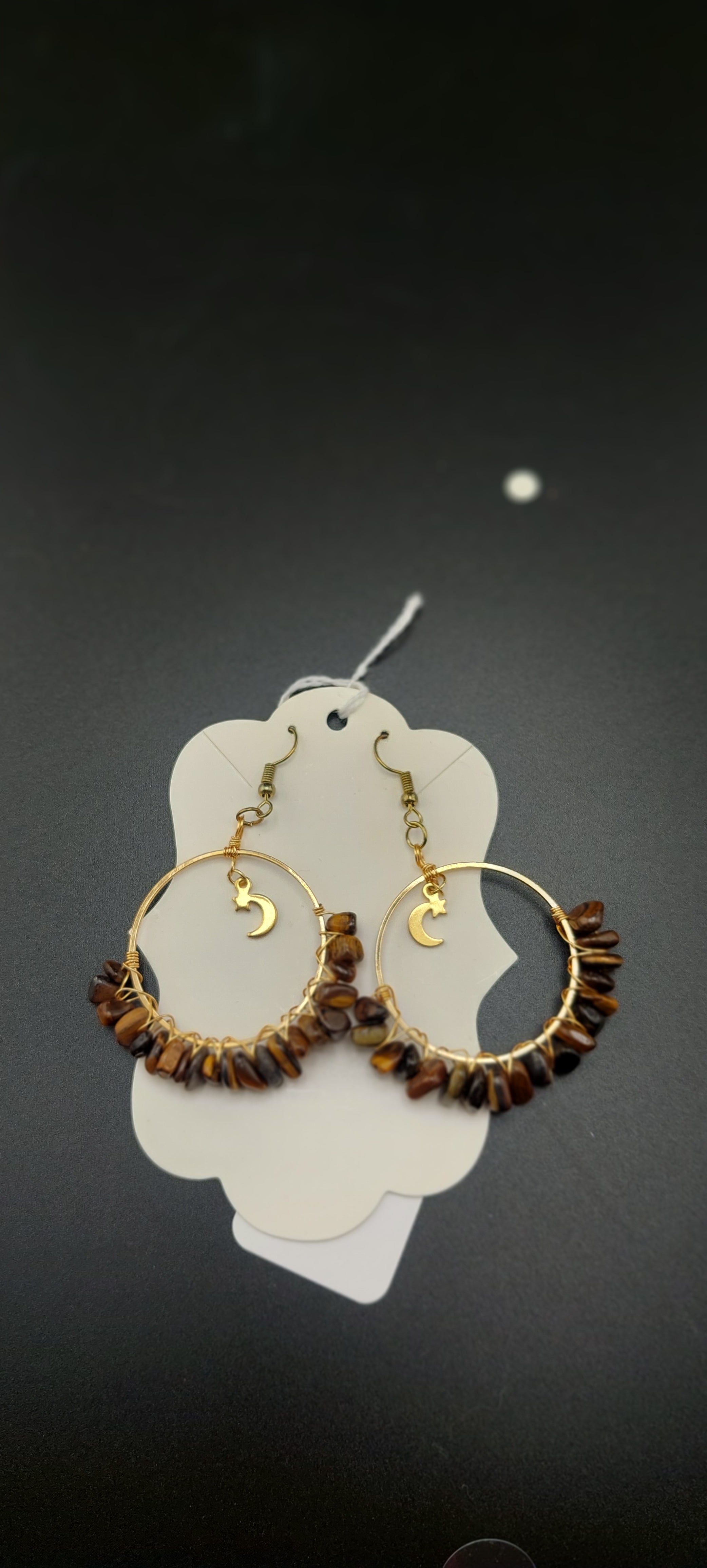 A pair of gold-colored hoop earrings with blue wire wrapping and dark blue beads, displayed on a white stand.
