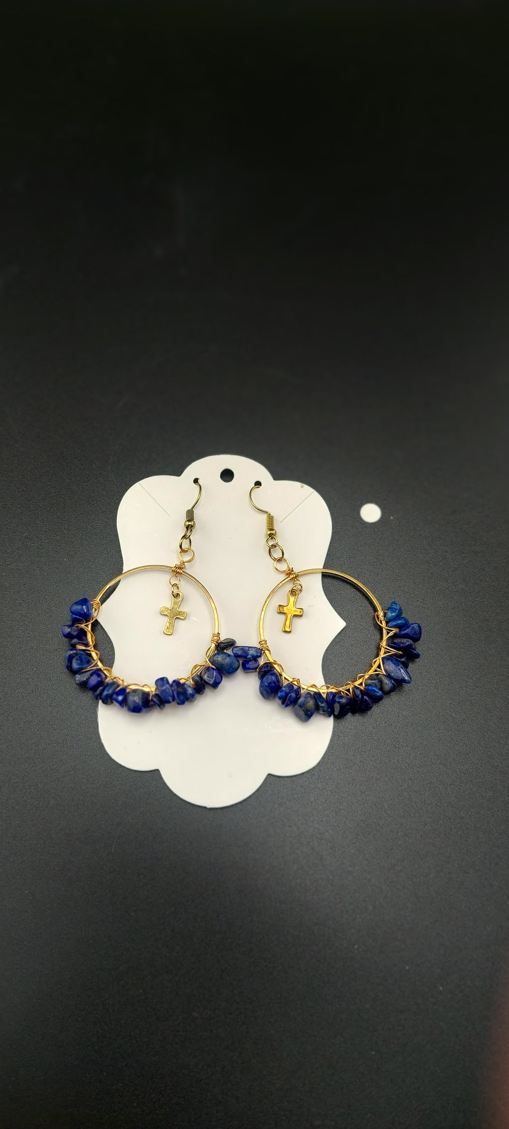 A pair of gold-colored hoop earrings with blue wire wrapping and dark blue beads, displayed on a white stand.