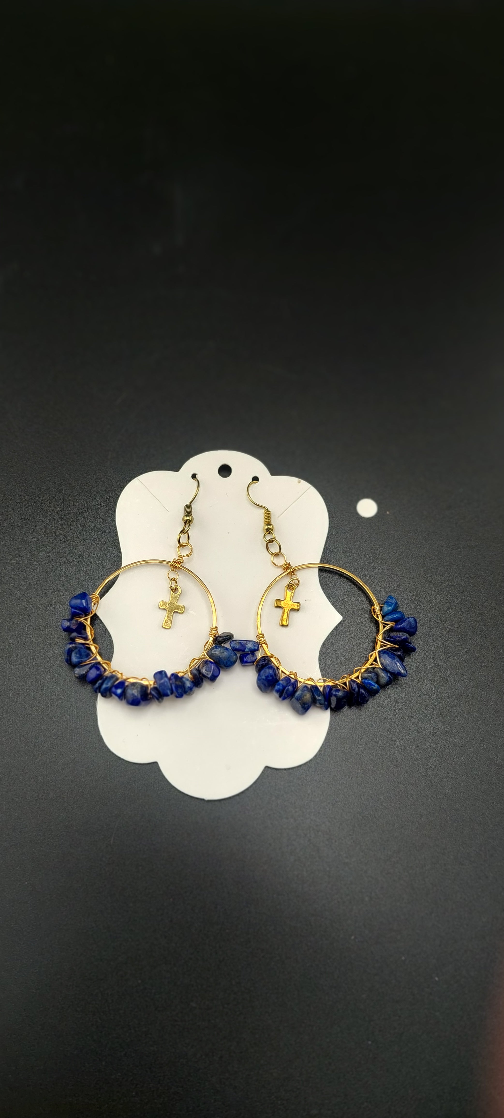 A pair of gold-colored hoop earrings with blue wire wrapping and dark blue beads, displayed on a white stand.
