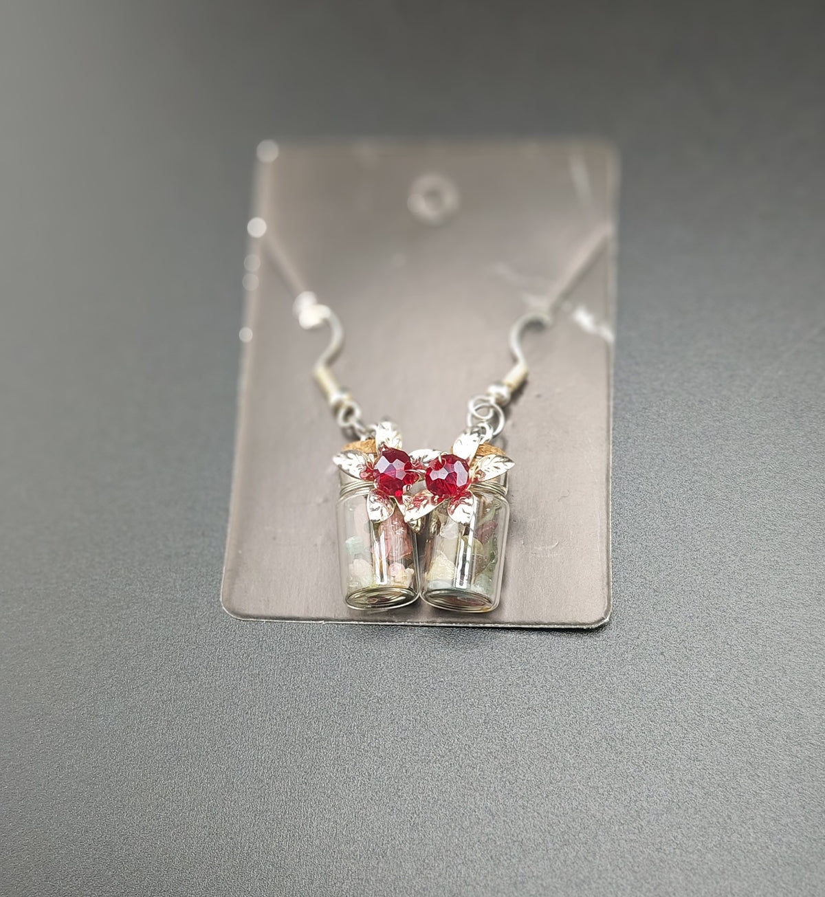 A pair of tourmaline bottle earrings with flower designs, mounted on a display card.