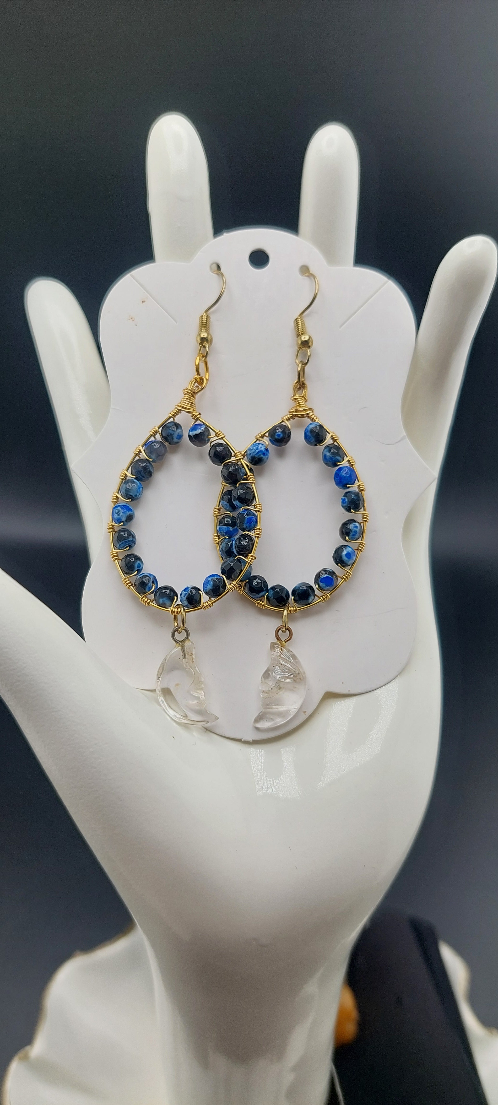 A pair of hoop earrings with blue orca beads, displayed on a white mannequin ear.