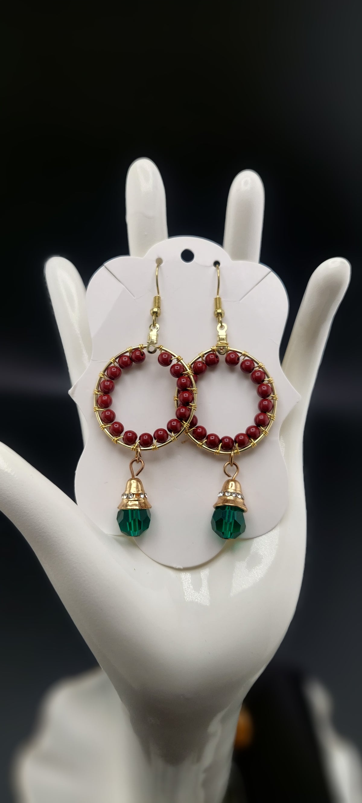 A pair of cinnabar hoop earrings with red and green colors displayed on a white mannequin ear.