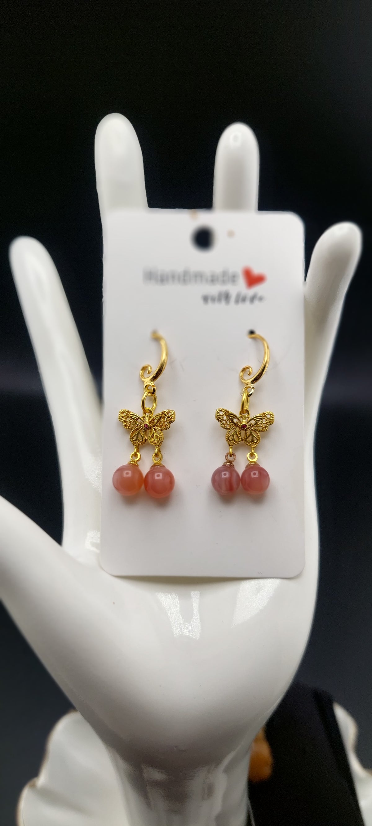 A pair of agate butterfly earrings displayed on a white mannequin ear stand, with the earrings featuring gold-colored butterflies and pink agate stones.