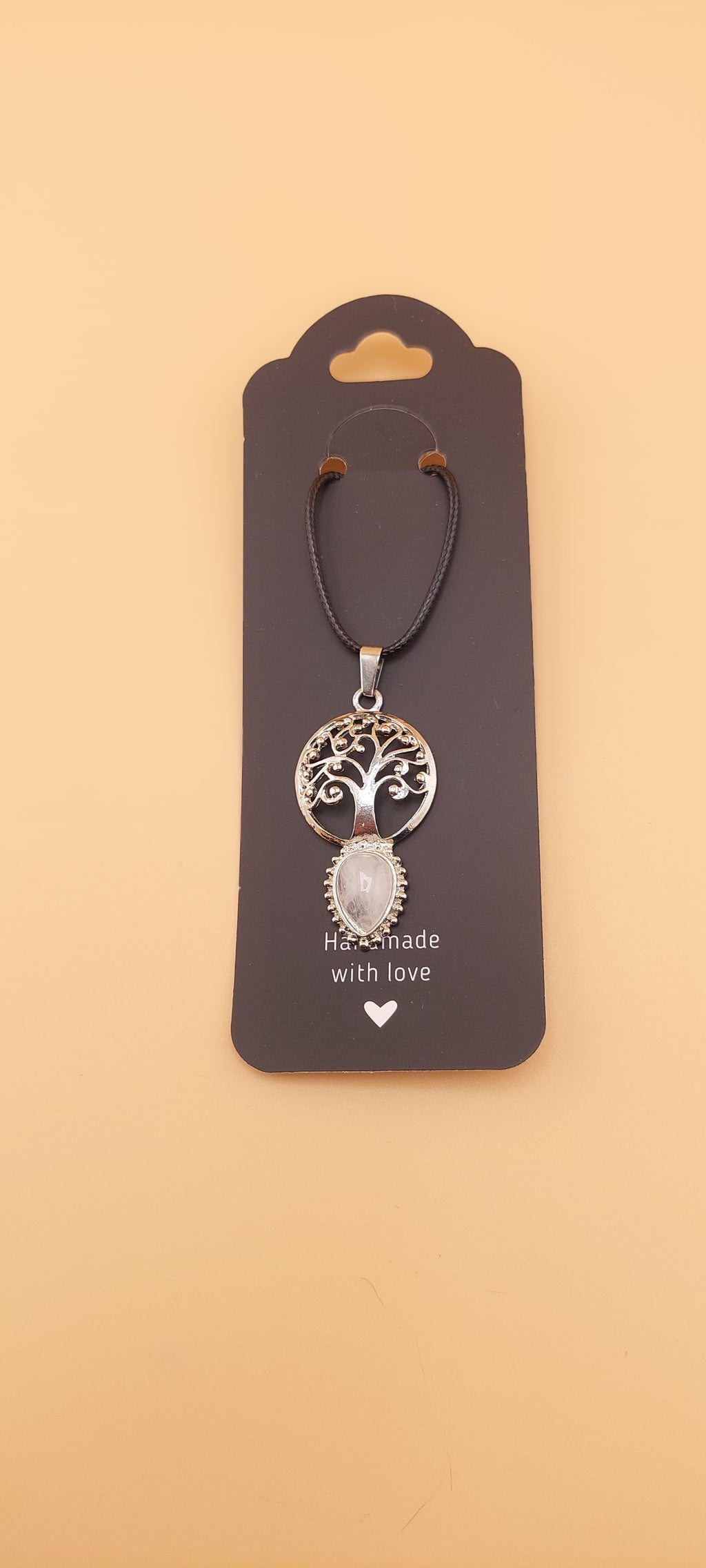 A Tree of Life necklace with a silver-colored design, displayed on a black card with a heart symbol.