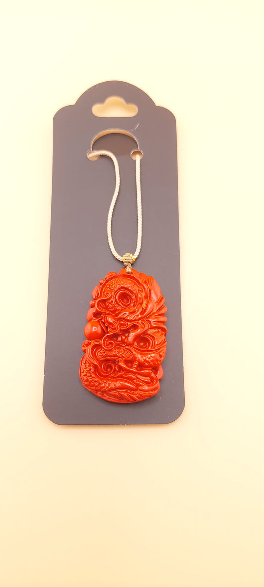 A red cinnabar necklace with a dragon design displayed on a grey card