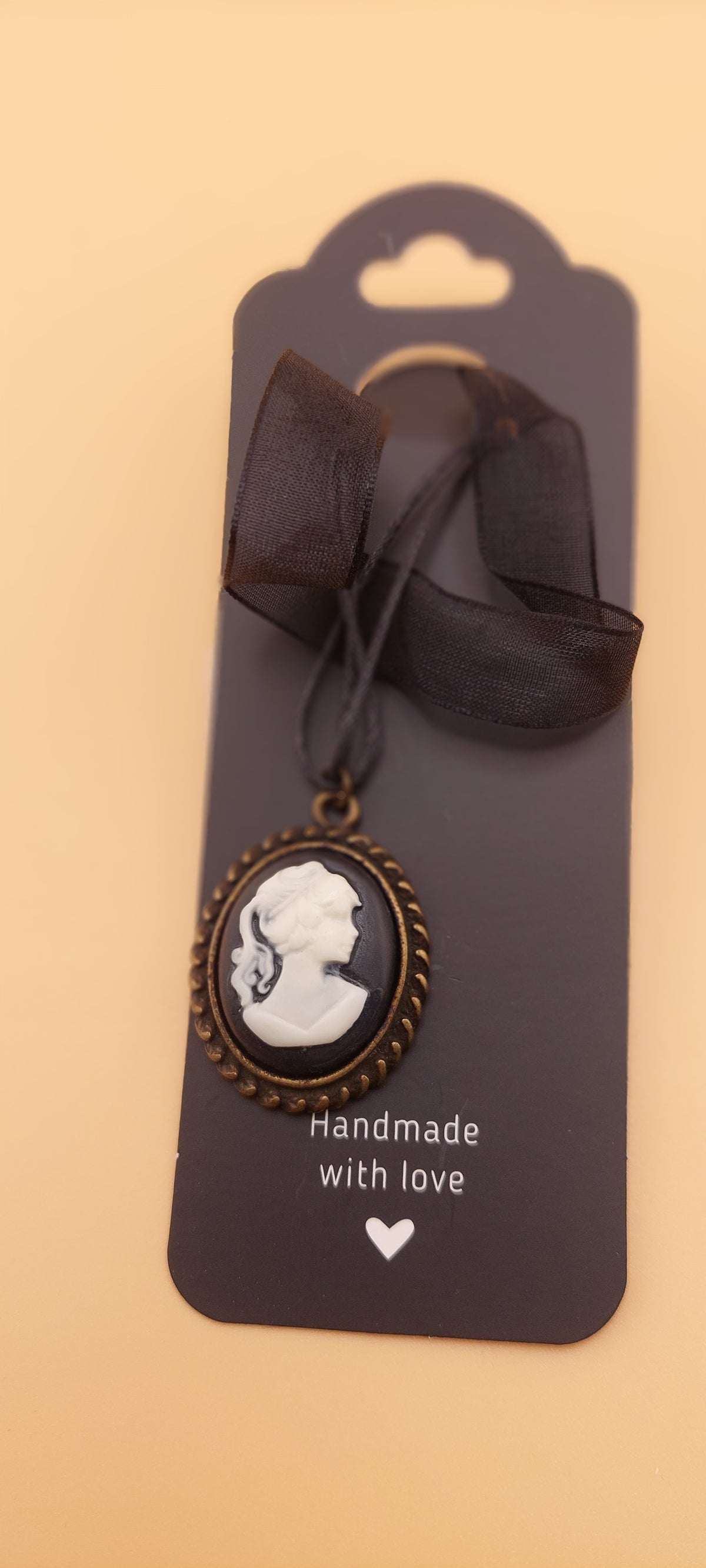 A black choker necklace with a white and black pendant, presented on a card that reads 'handmade with love'.