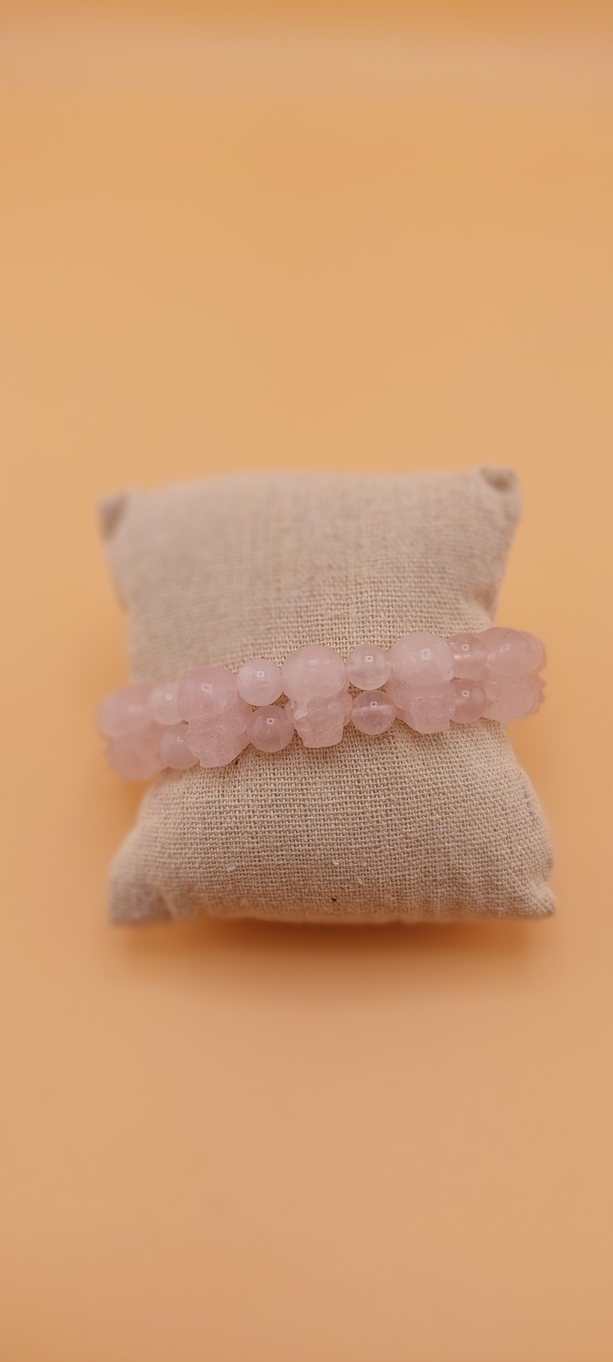 A rose quartz pixiu bracelet displayed on a beige cushion against an orange background.