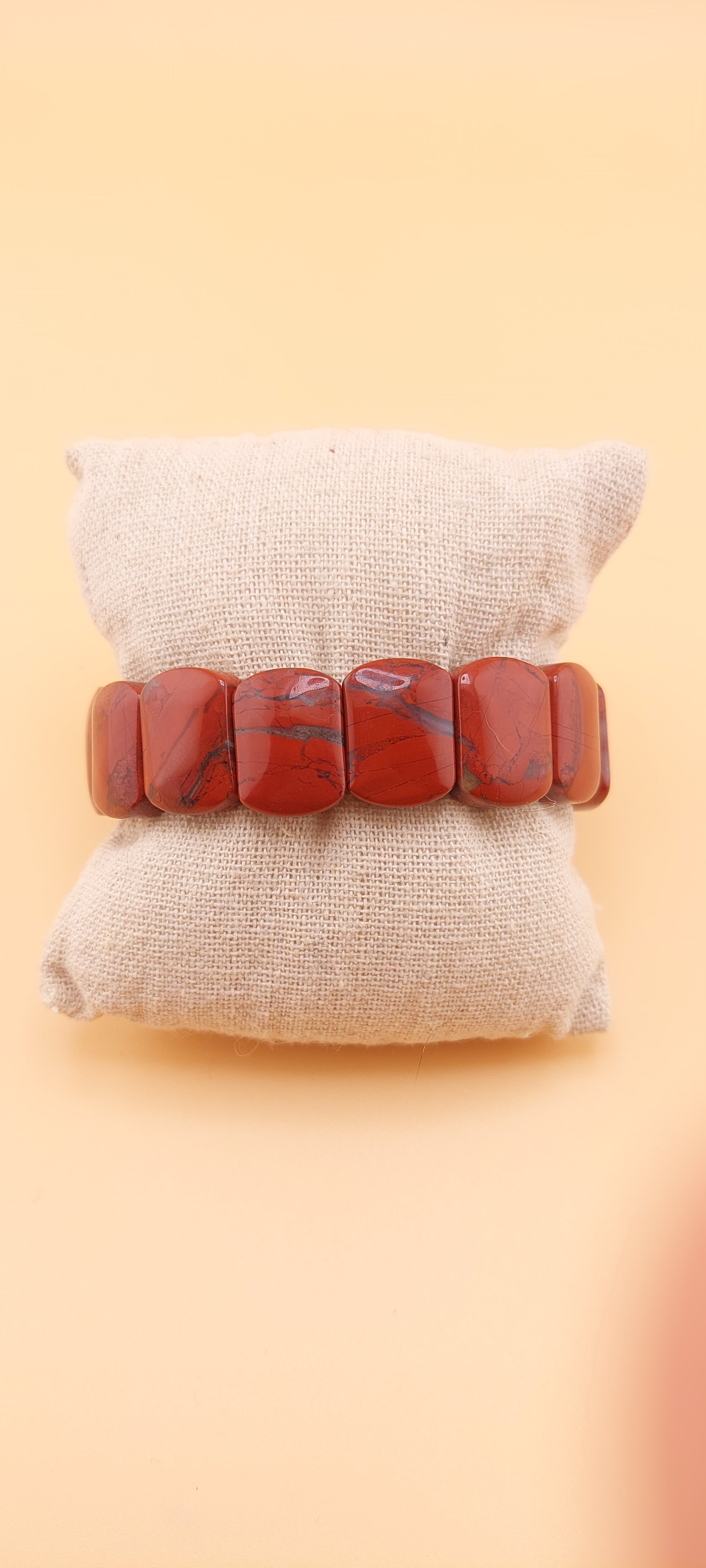 A red jasper soft bangle displayed on a beige cushion against a yellow background.
